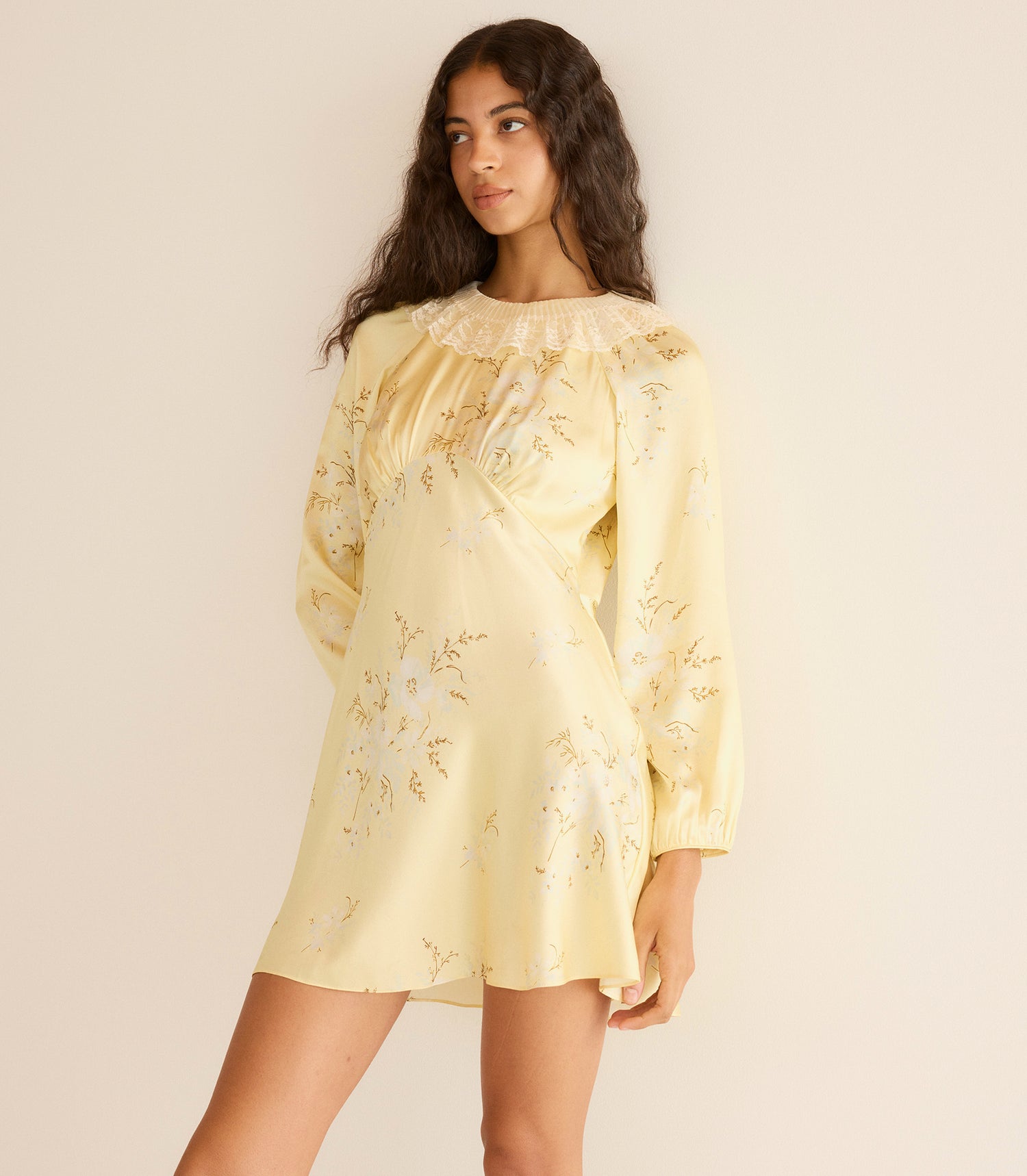 Woman wearing a light yellow floral dress against a beige background