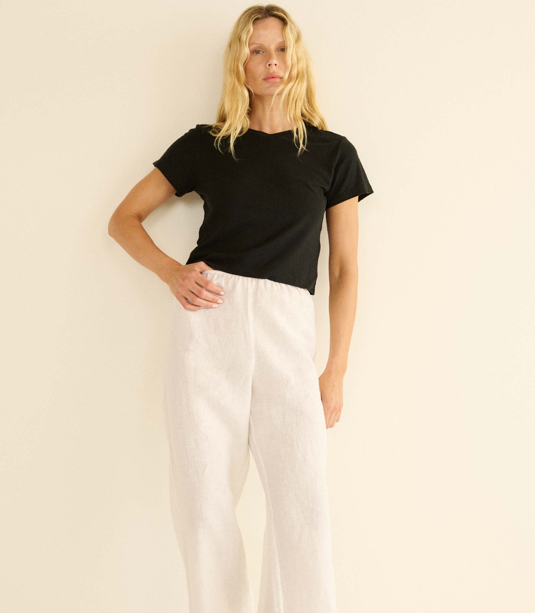 Woman wearing a black t-shirt and white pants against a beige background 2
