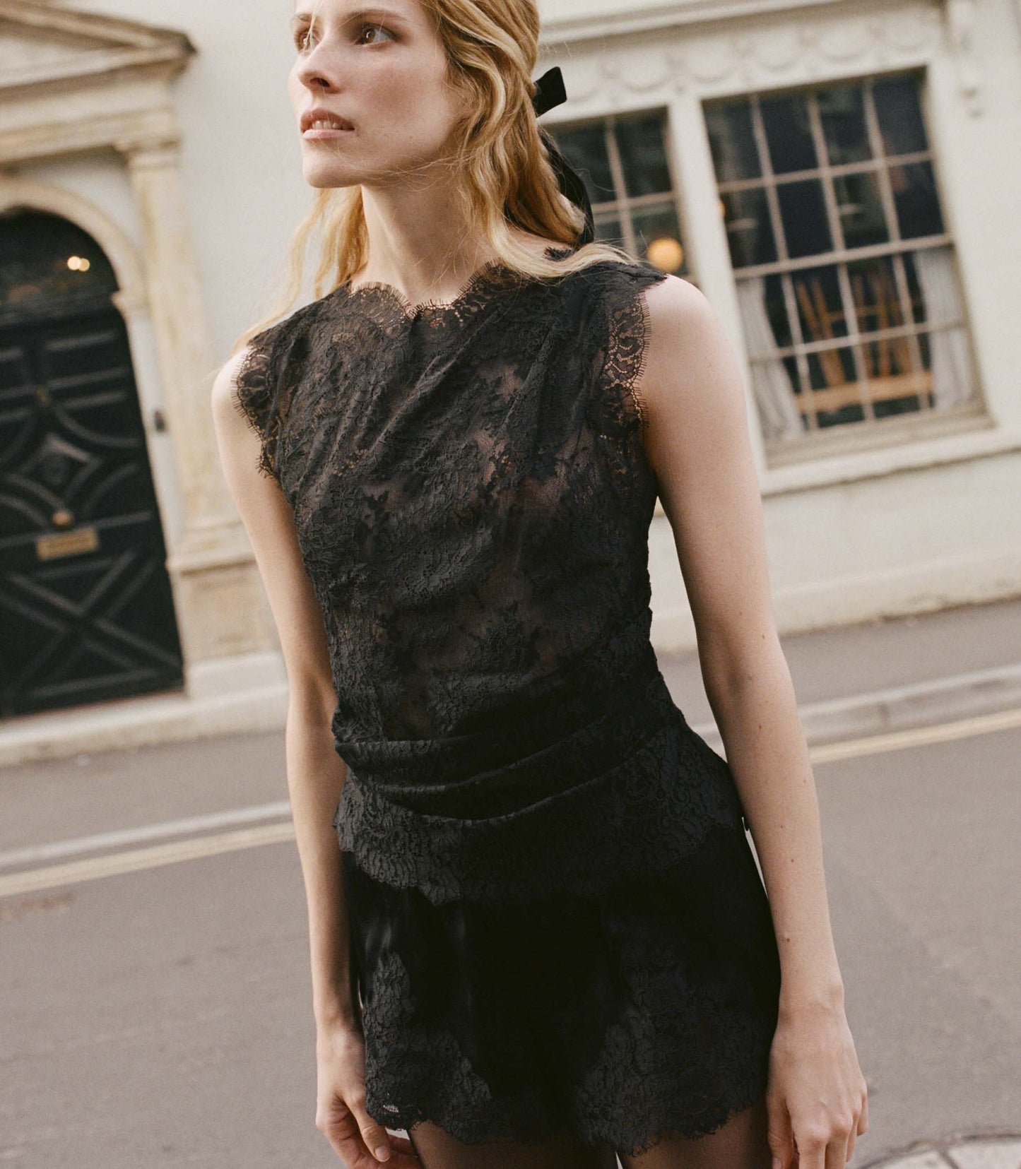Woman wearing a black lace top standing on a street.