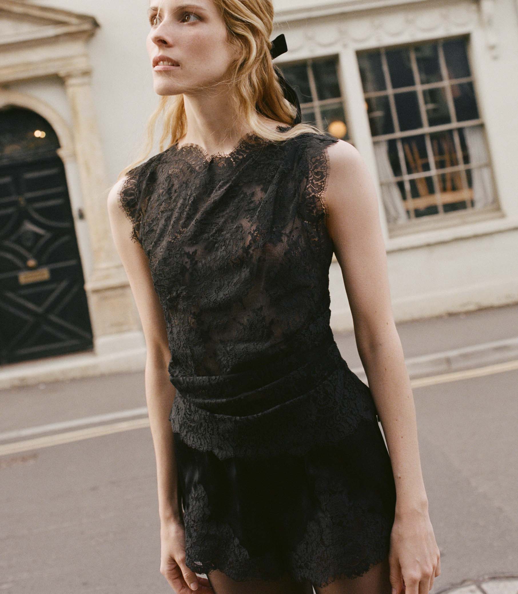 Woman wearing a black lace top standing on a street. 1