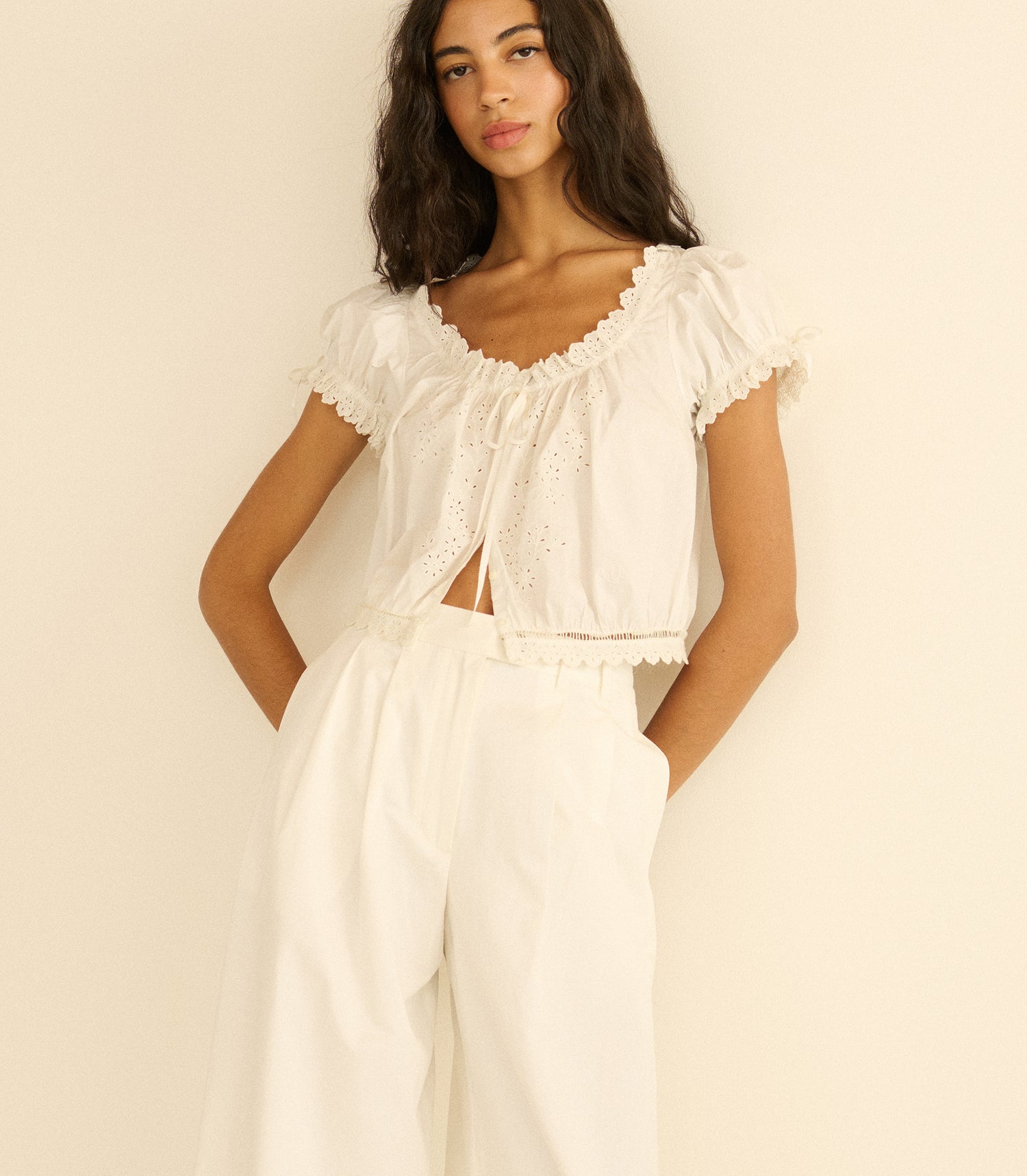 Woman wearing a white outfit with ruffled top and wide-leg pants against a beige background