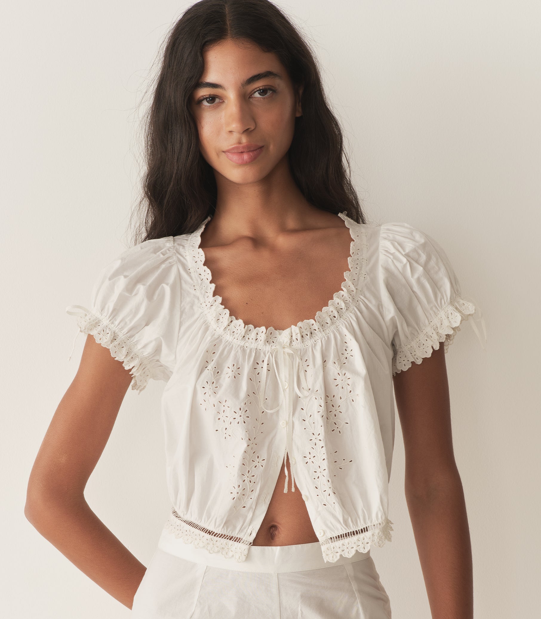 Rocio is wearing a white short puff sleeve top with white pants and yellow mule heels.