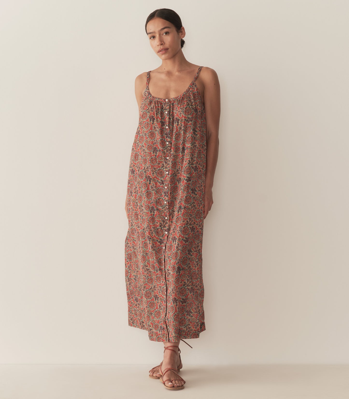 Zahara is wearing a sleeveless midi dress in an orange floral pattern, paired with sandals.