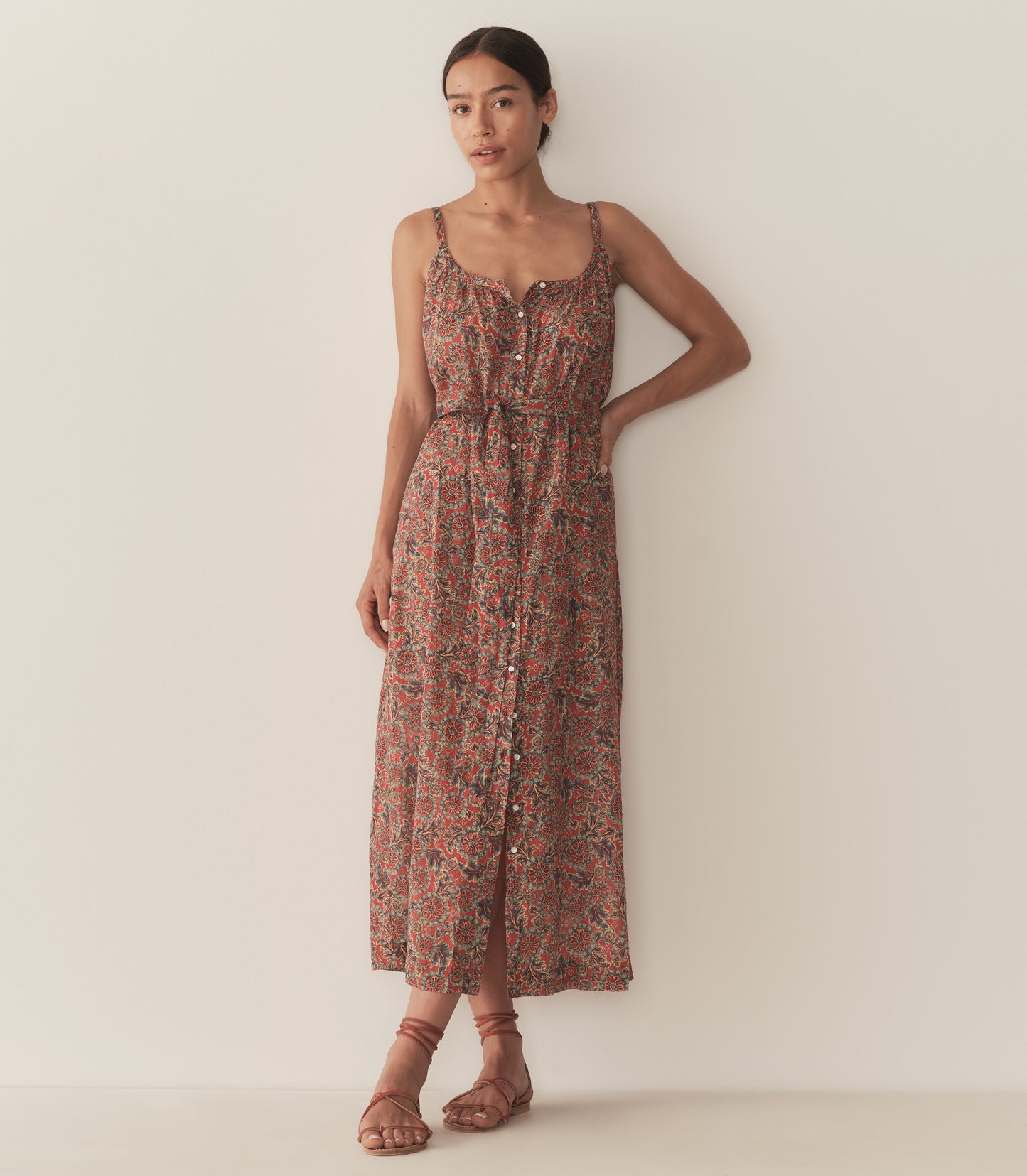 Zahara is wearing a sleeveless midi dress in an orange floral pattern, paired with sandals.