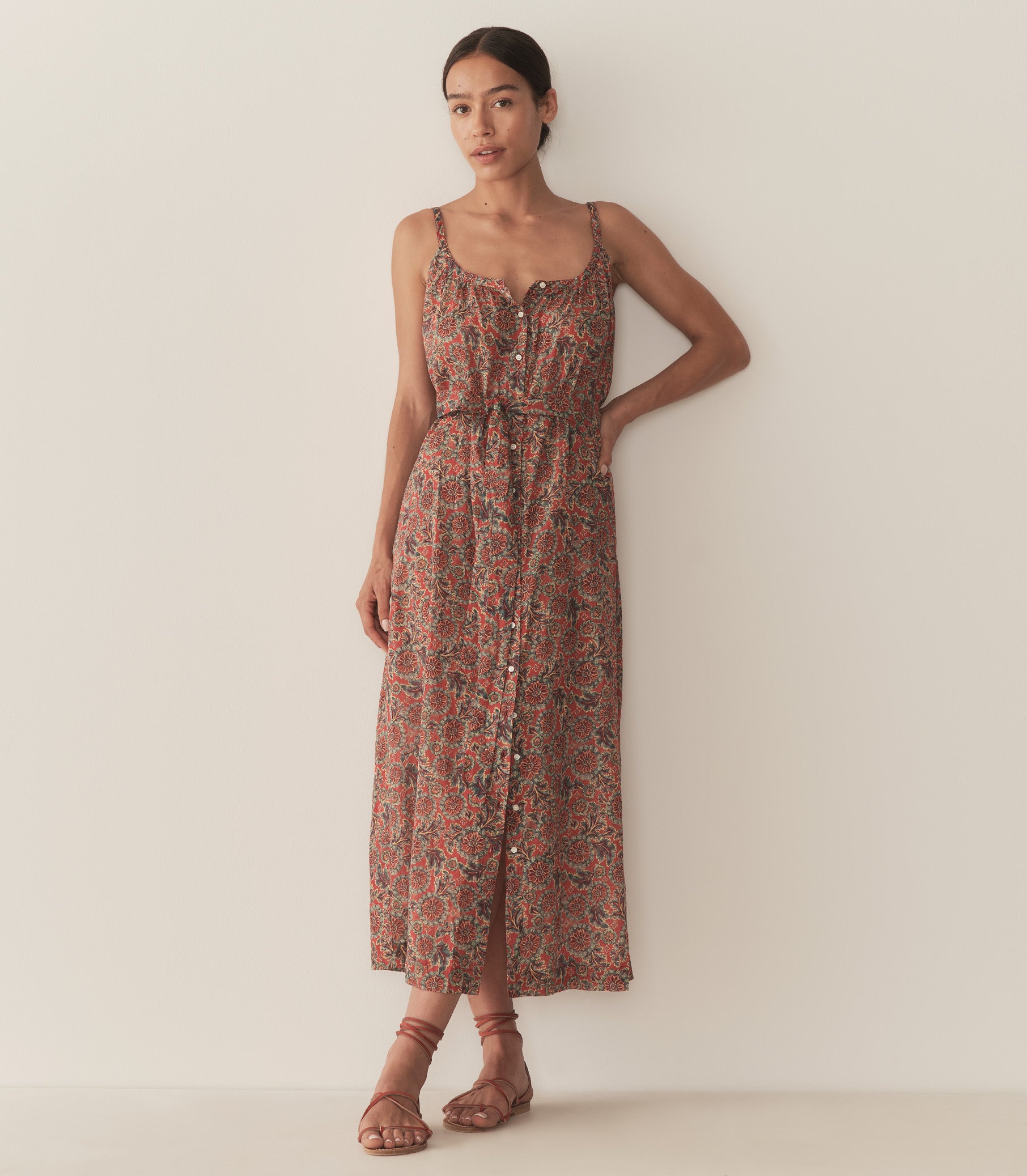 Zahara is wearing a sleeveless midi dress in an orange floral pattern, paired with sandals.