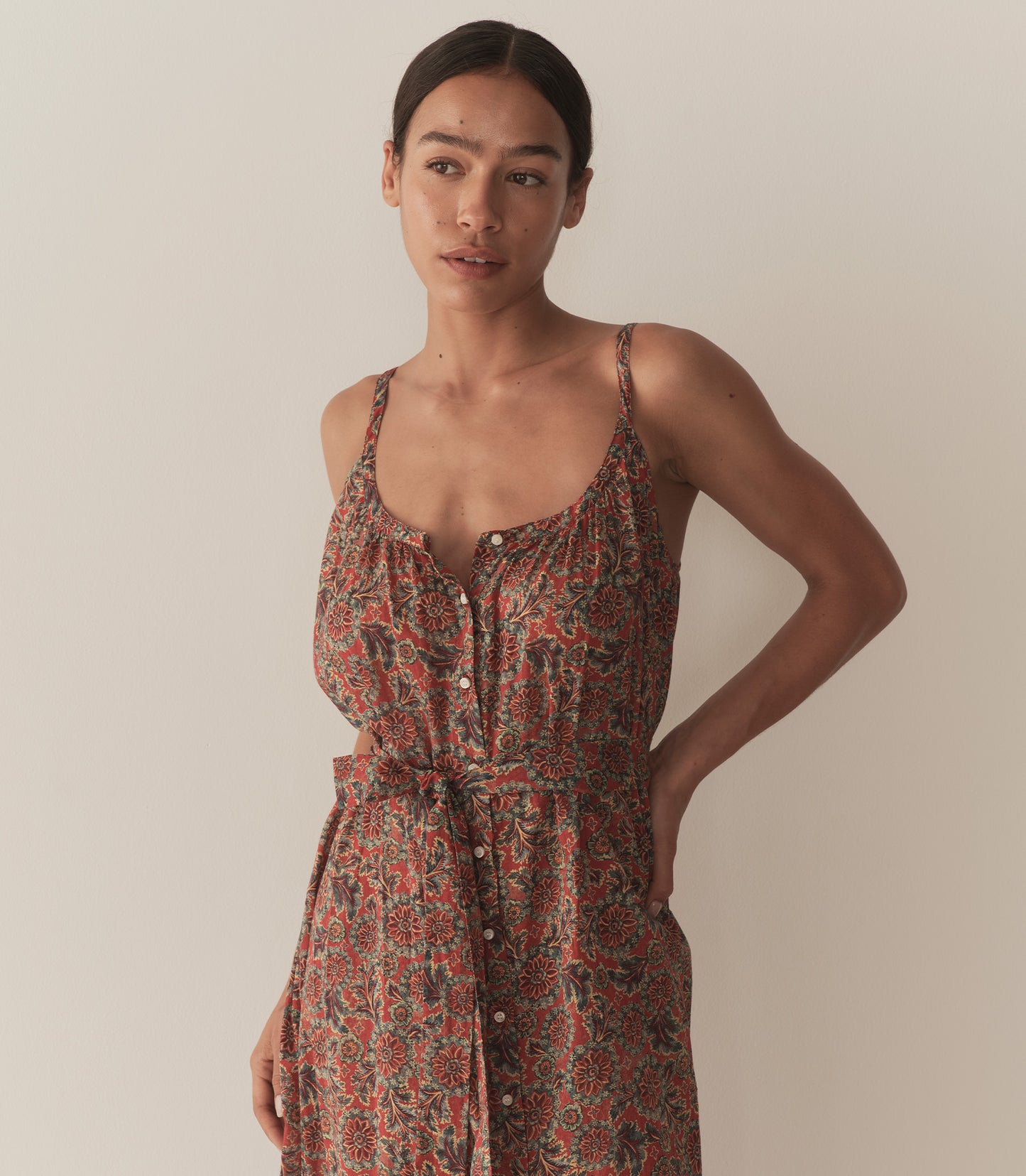 Zahara is wearing a sleeveless midi dress in an orange floral pattern, paired with sandals.