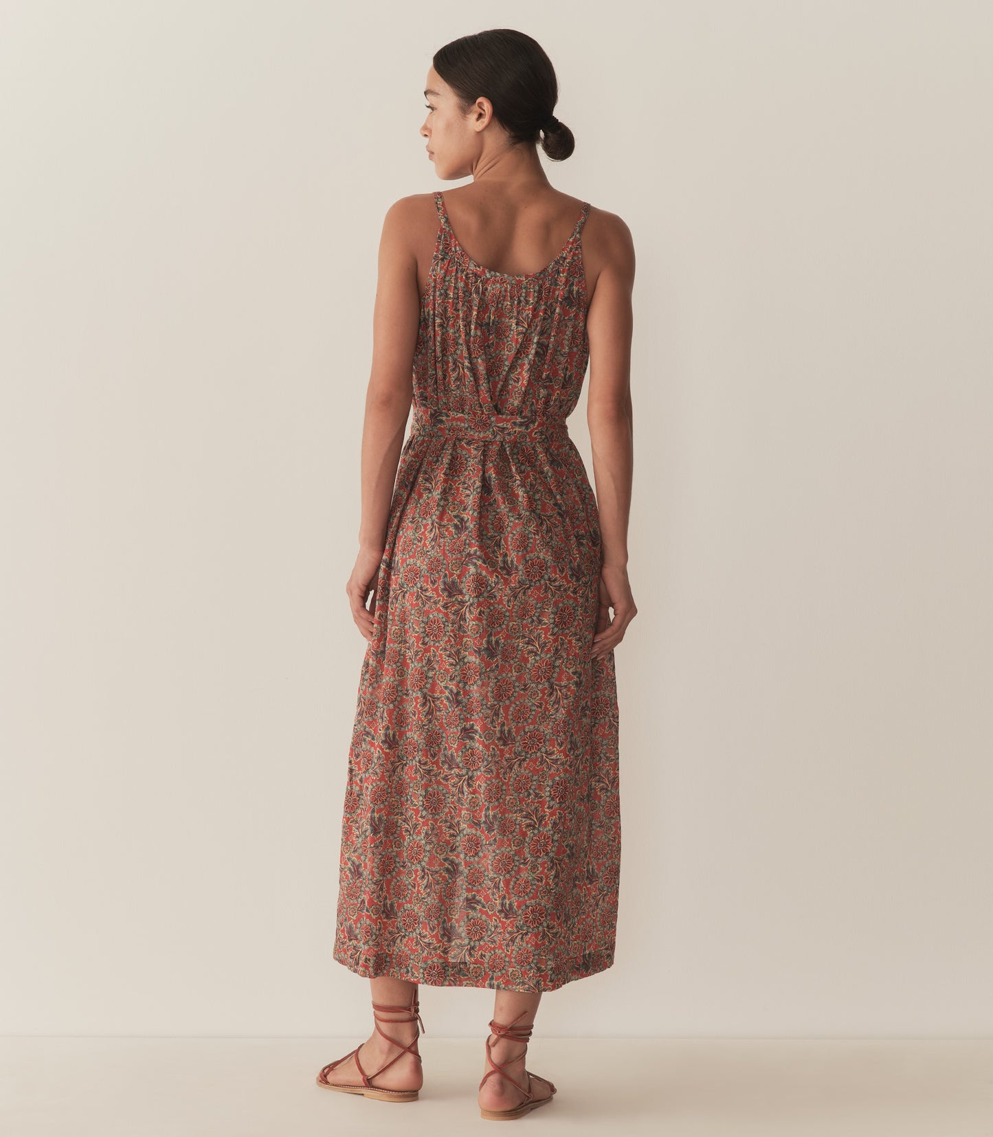 Zahara is wearing a sleeveless midi dress in an orange floral pattern, paired with sandals.