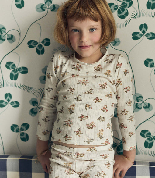 Young girl in a floral matching set standing against a patterned wall.