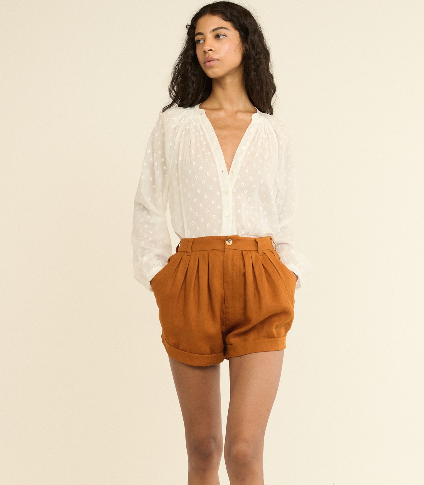 Woman wearing a white blouse and brown shorts on a beige background