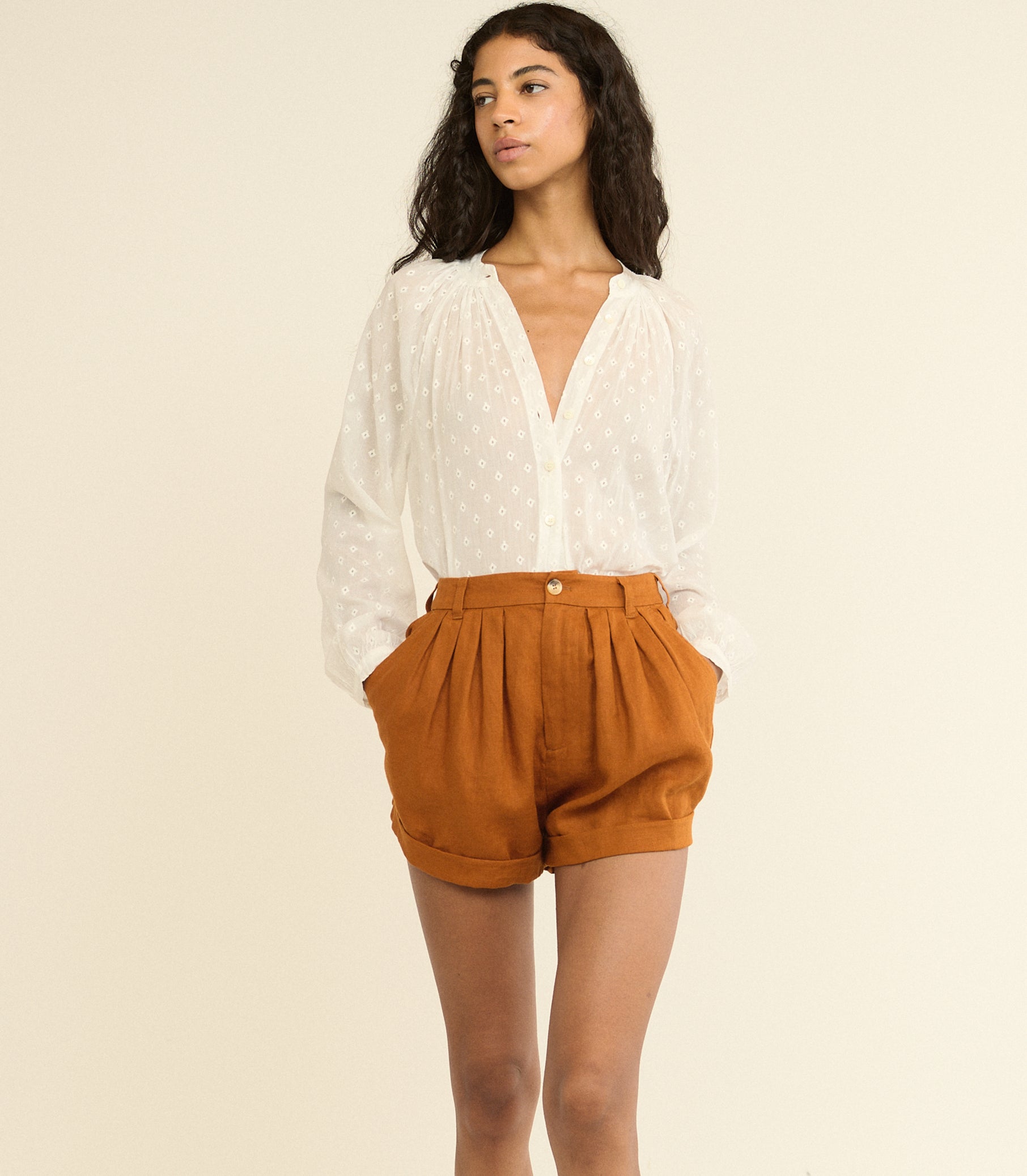 Woman wearing a white blouse and brown shorts on a beige background 1
