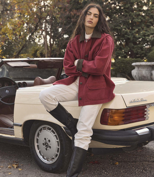 Woman in a red coat sitting on the back of a vintage car with trees in the background