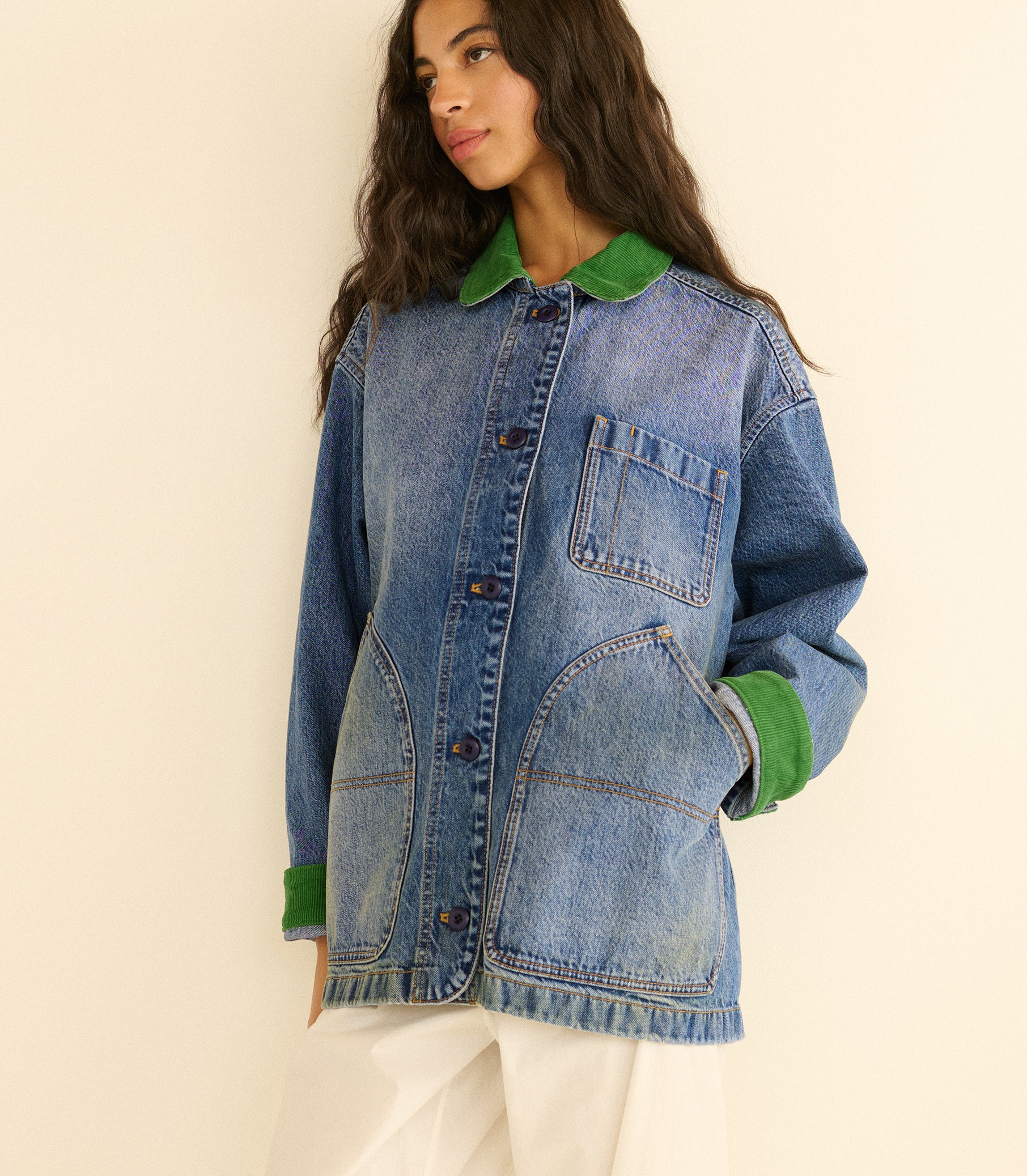 Person wearing a blue denim jacket with green collar and cuffs on a beige background 1
