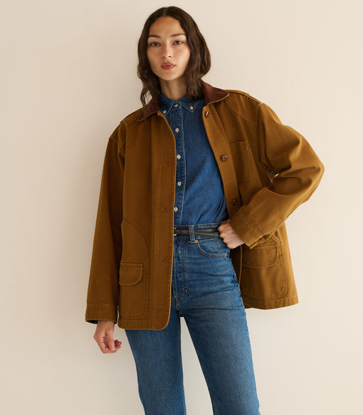 Woman wearing a brown jacket and blue jeans against a plain background