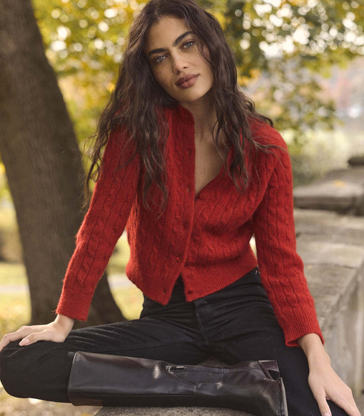 Woman wearing a red cardigan sitting outdoors with blurred greenery in the background