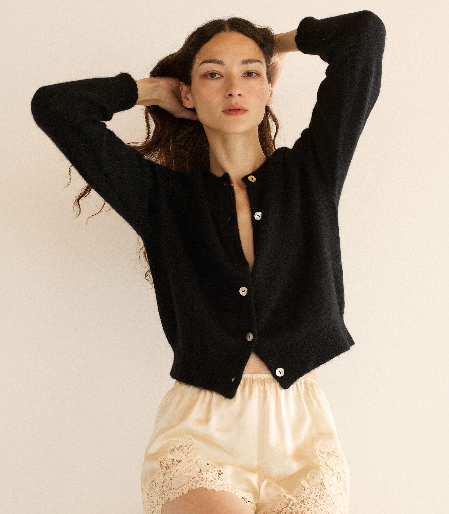 Woman wearing a black cardigan over a beige top with lace details on a plain background