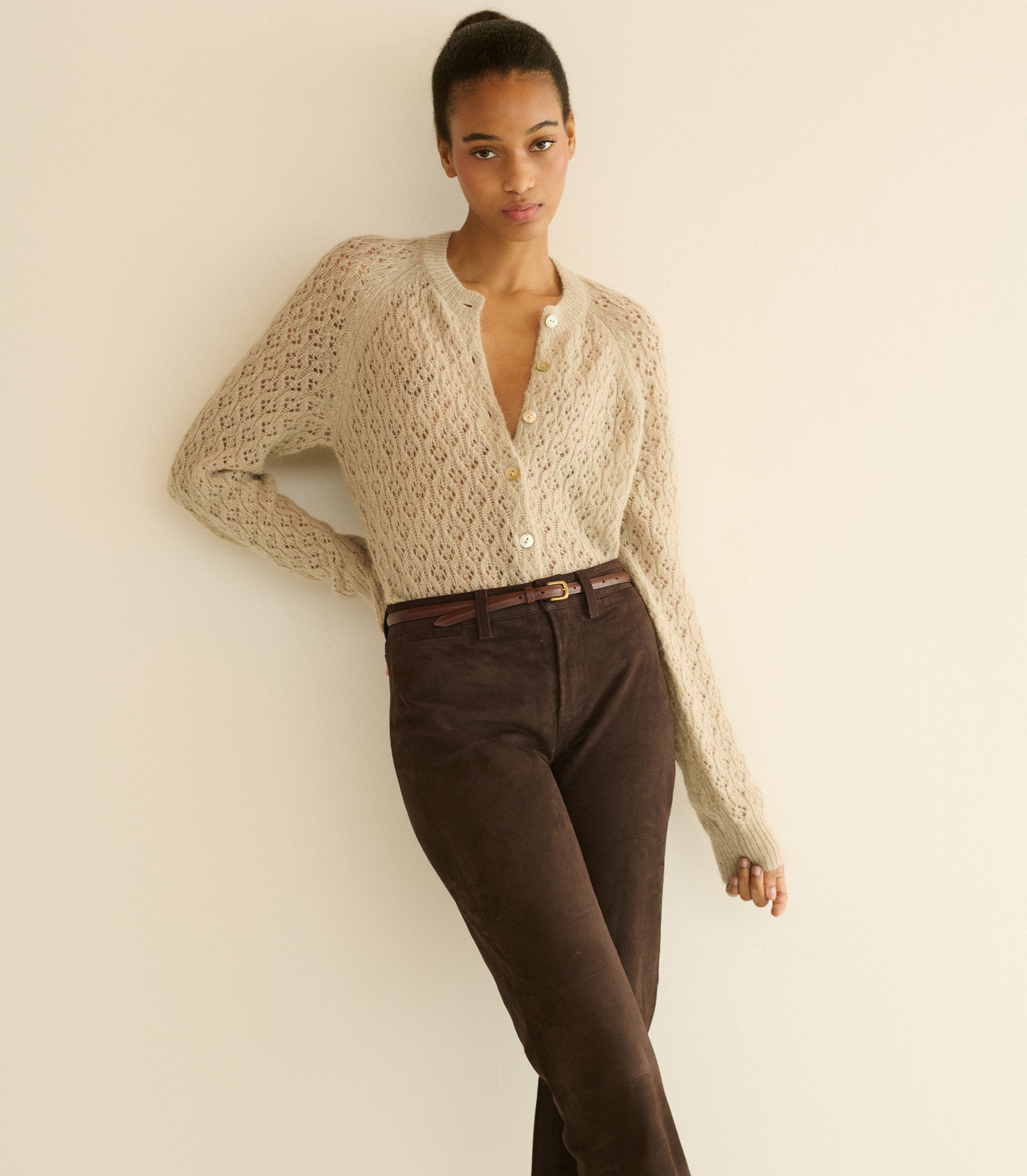 Woman wearing a beige cardigan and brown pants against a plain background