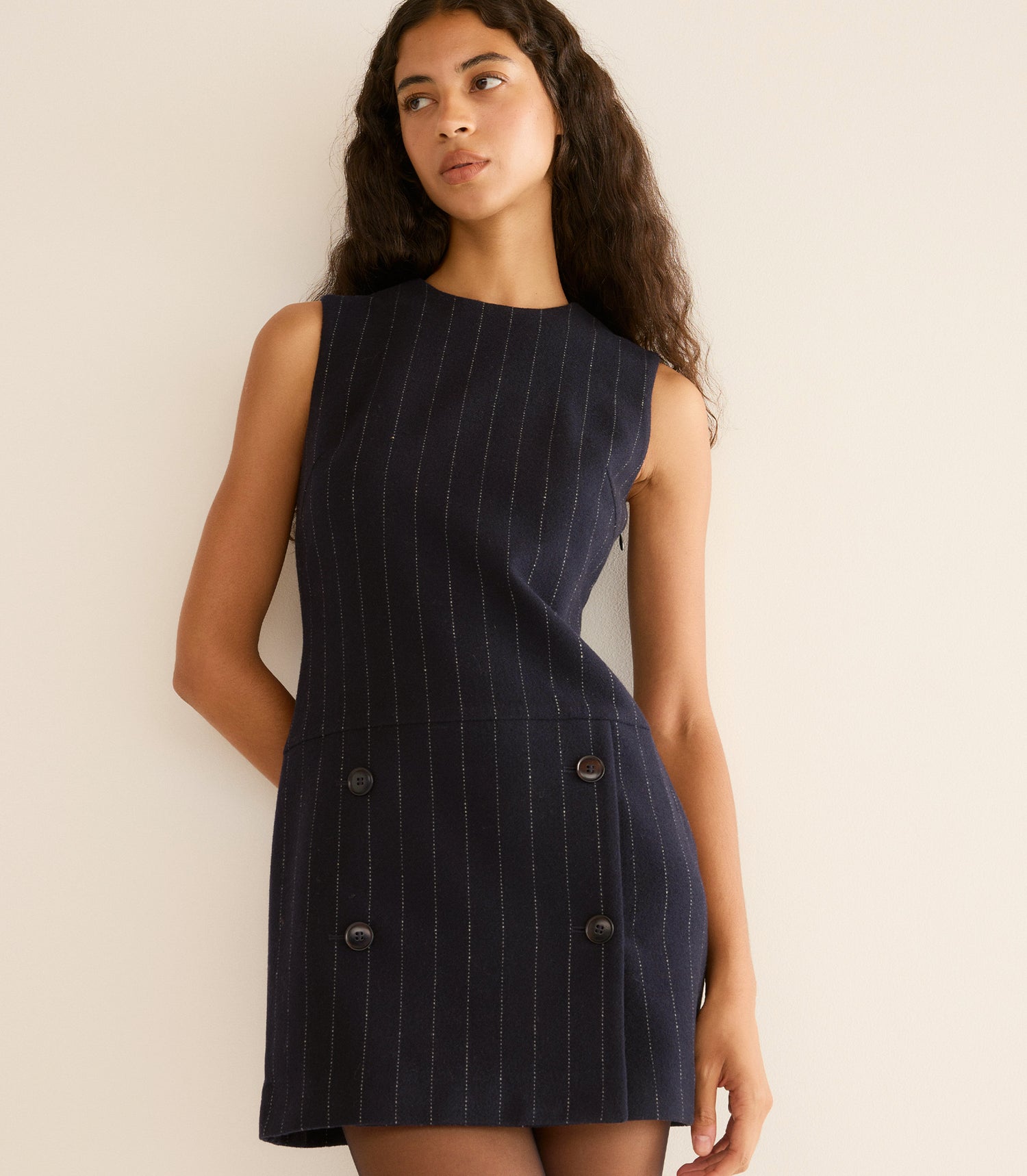 Woman wearing a navy pinstripe dress against a beige background