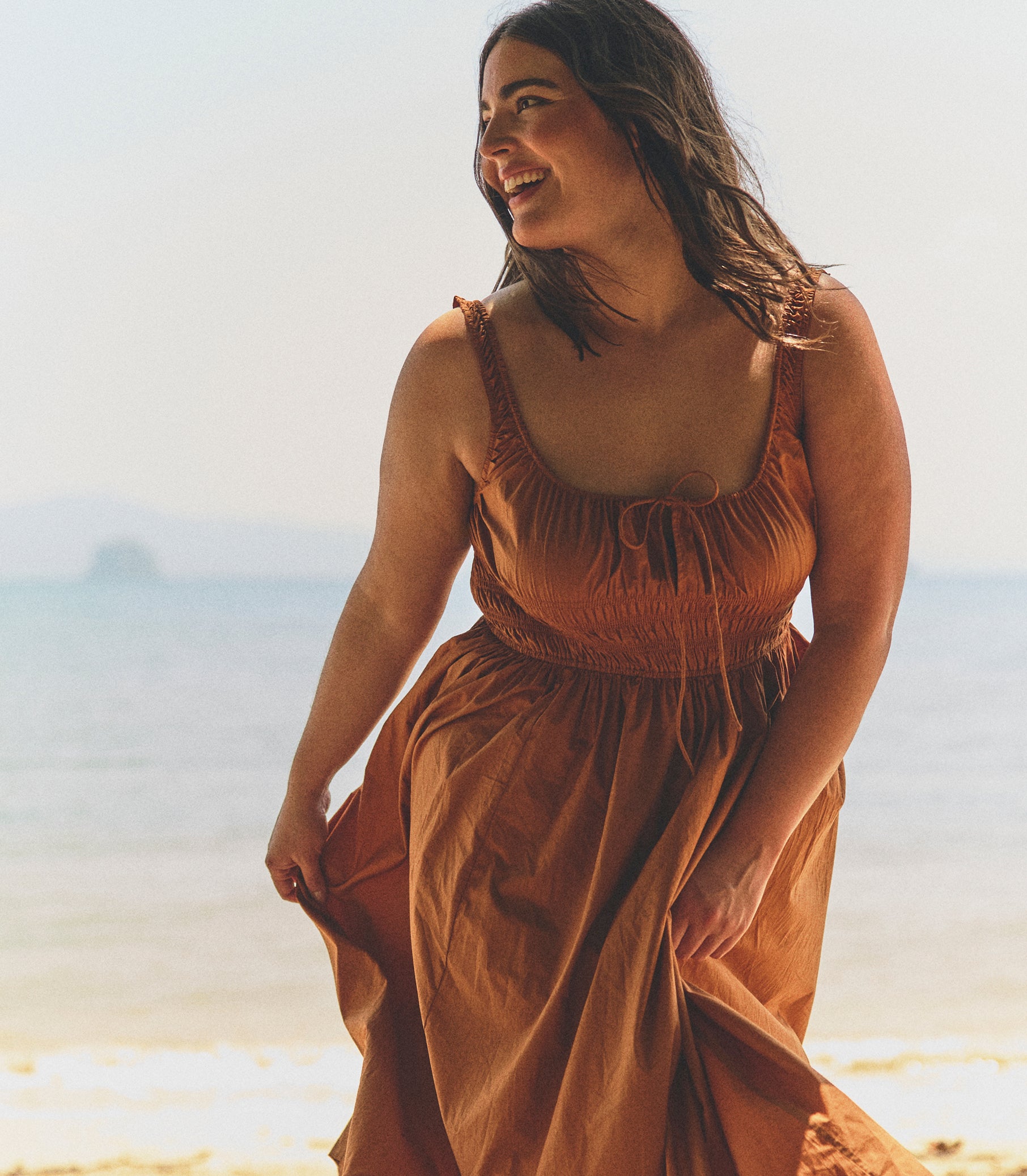 Woman in a rust-colored dress standing on a beach with a blurred background 1
