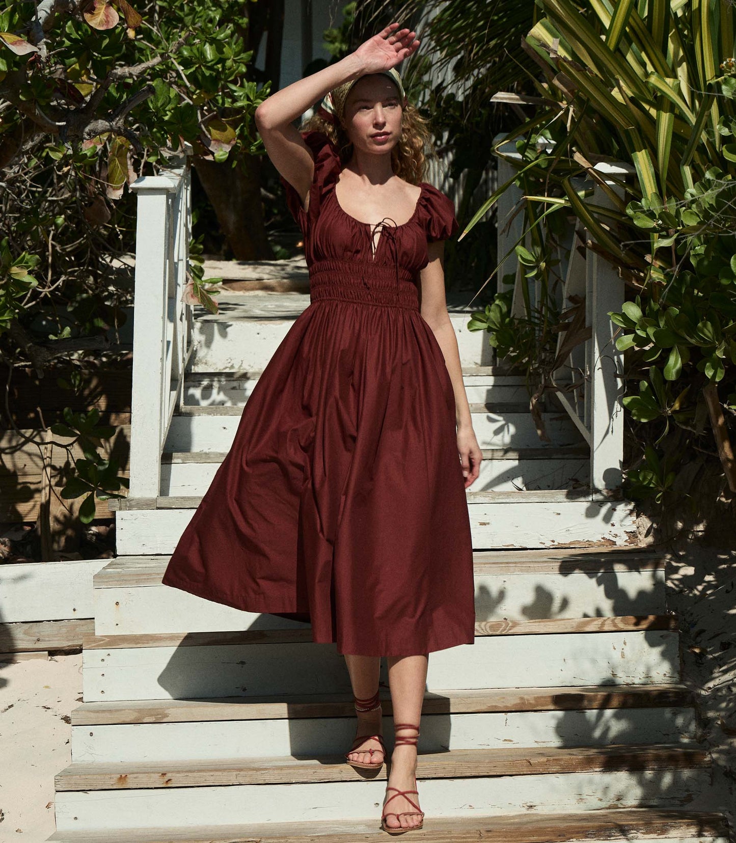 Heloise is wearing a burgundy short puff sleeved midi dress with sandals and a bandana.