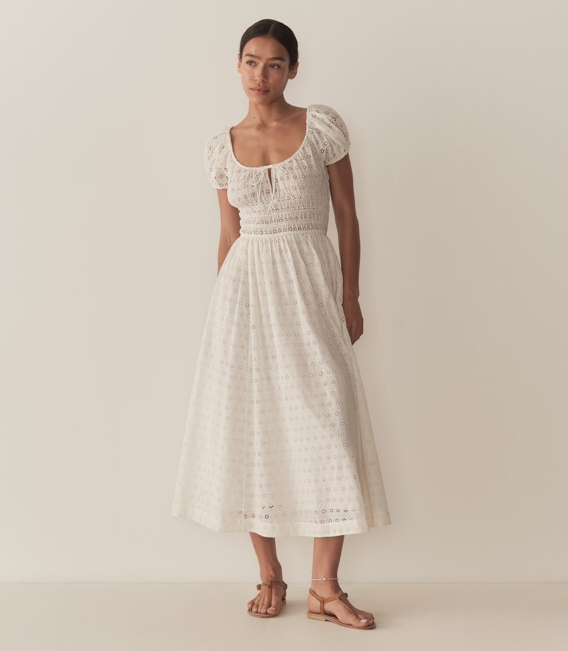 Zahara wears a long white eyelet dress with short puff sleeves, paired with tan sandals. 1