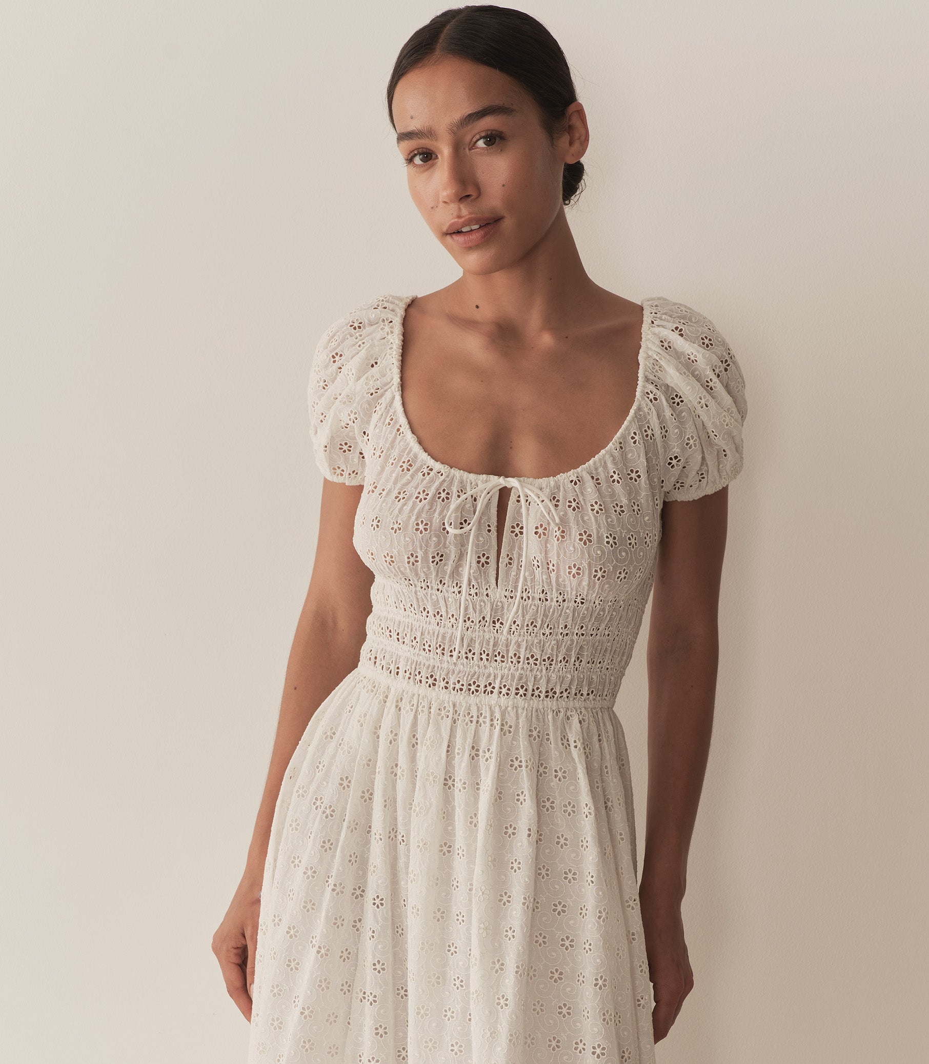 Zahara wears a long white eyelet dress with short puff sleeves, paired with tan sandals. 2
