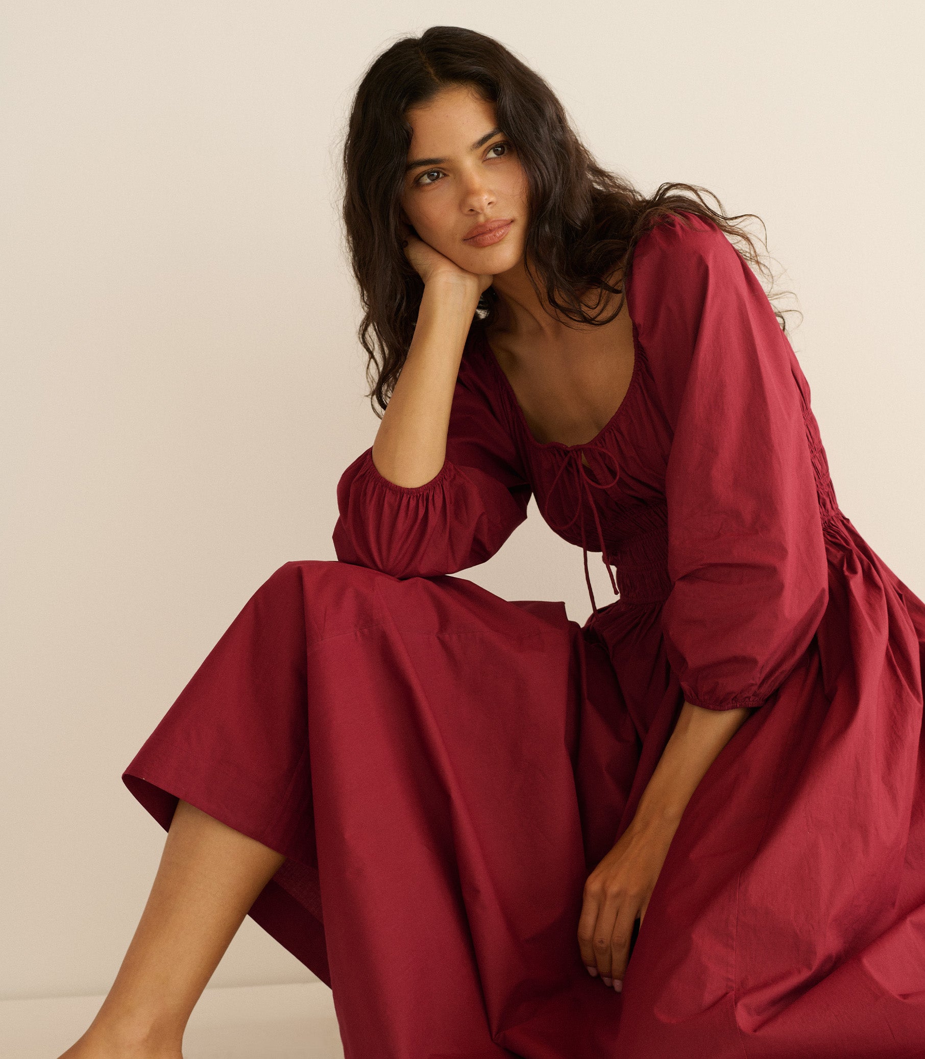 Woman wearing a burgundy dress sitting against a plain background