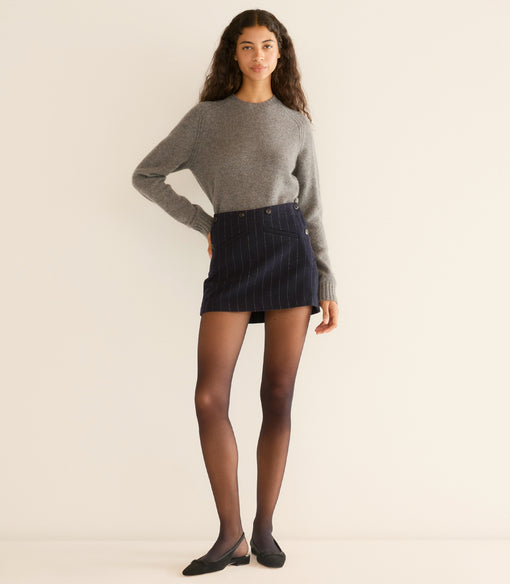 Woman wearing a gray sweater and navy skirt on a beige background