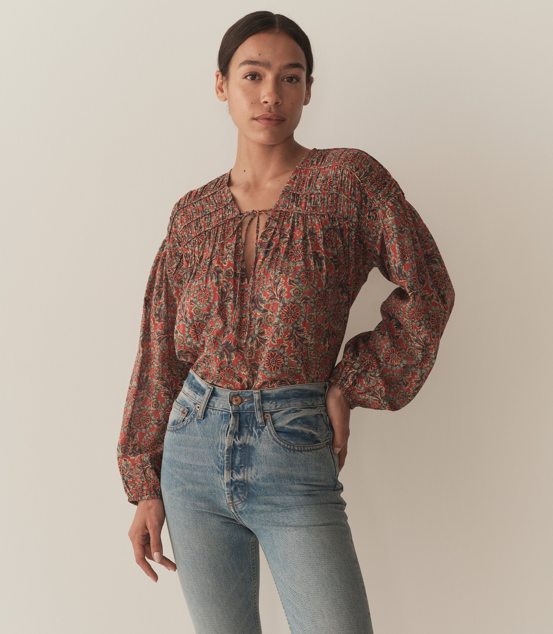 Zahara wears a burnt orange floral blouse fashioned with long balloon sleeves and paired with blue jeans.