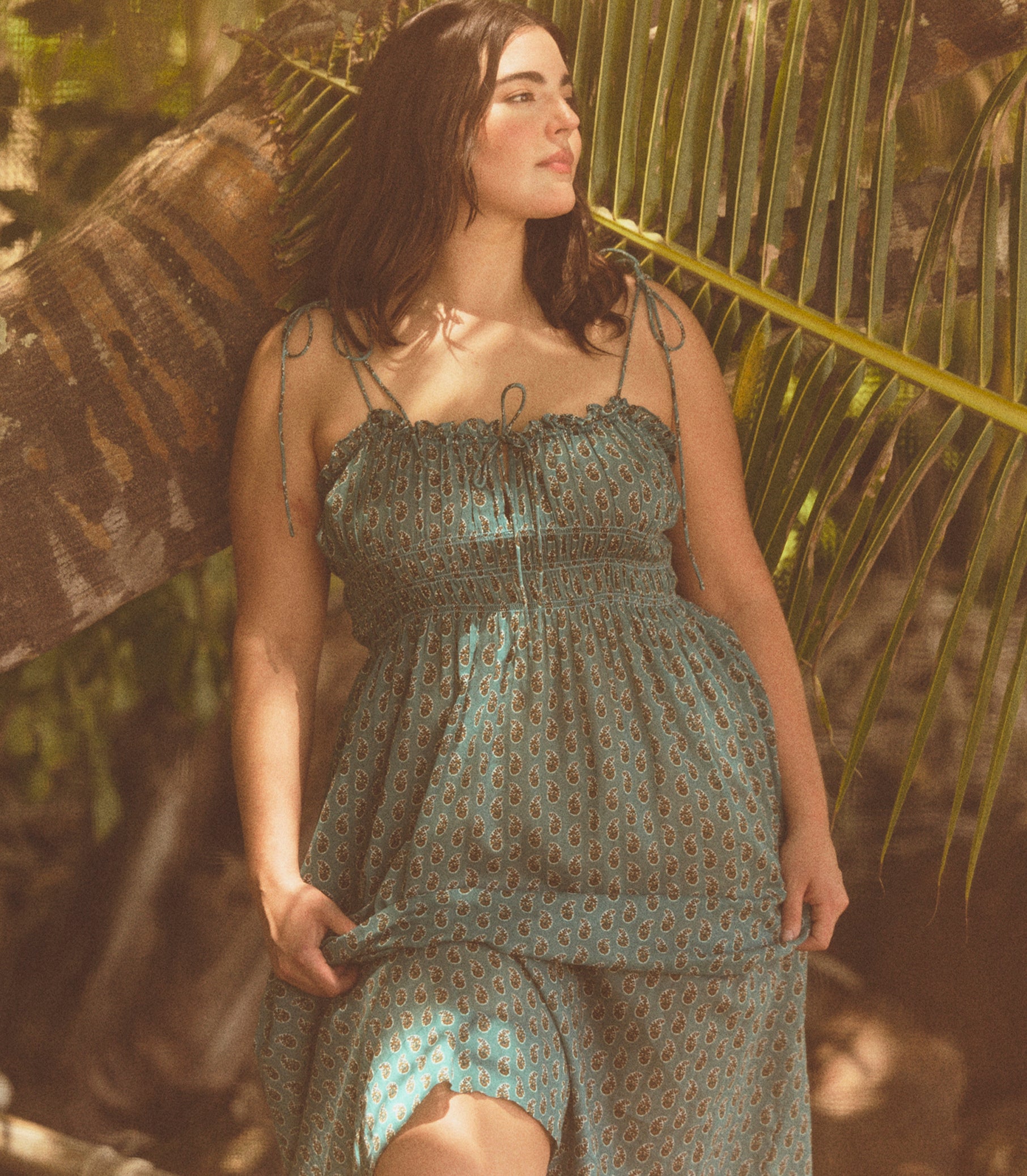 Woman in a green patterned dress standing among palm leaves 1
