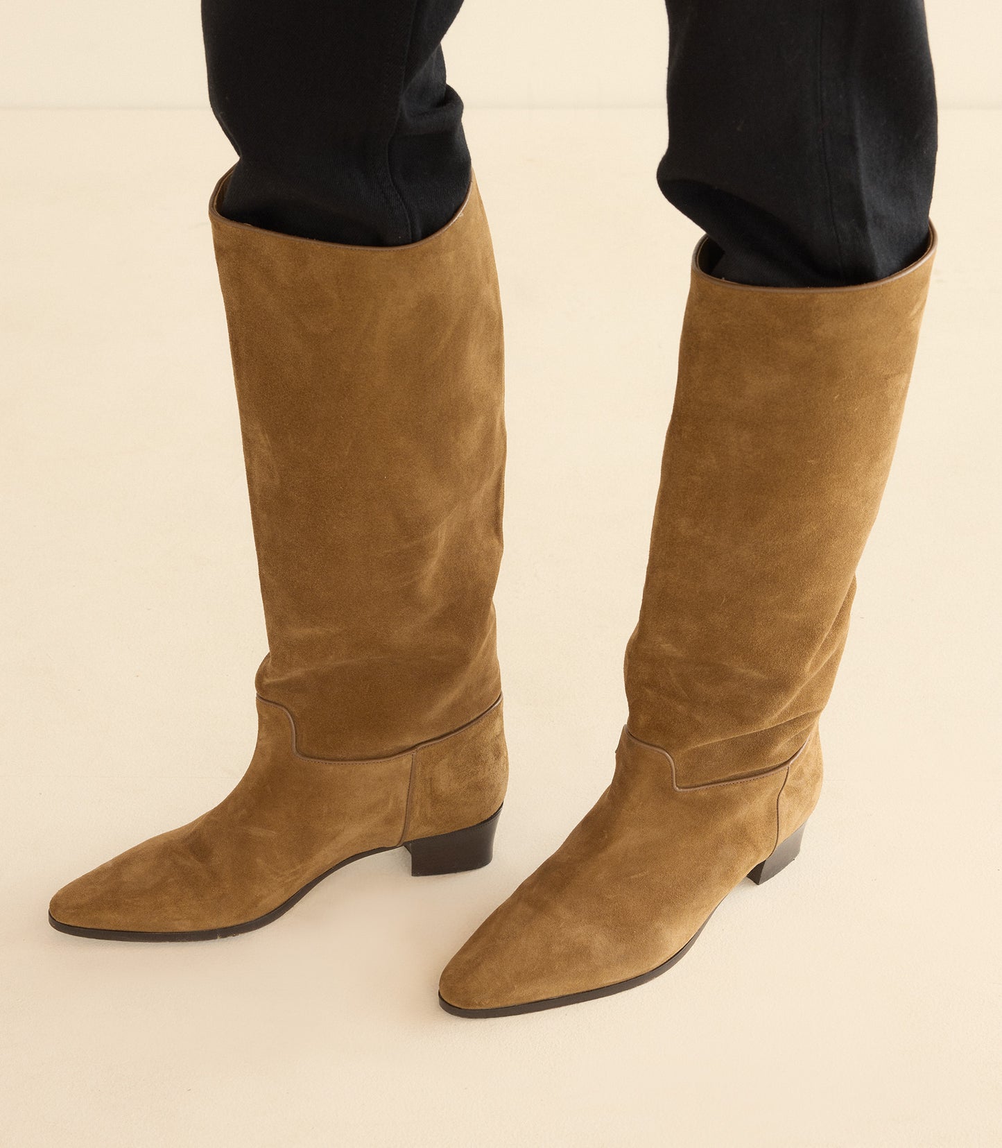 Tan knee-high boots worn with dark pants on a light background