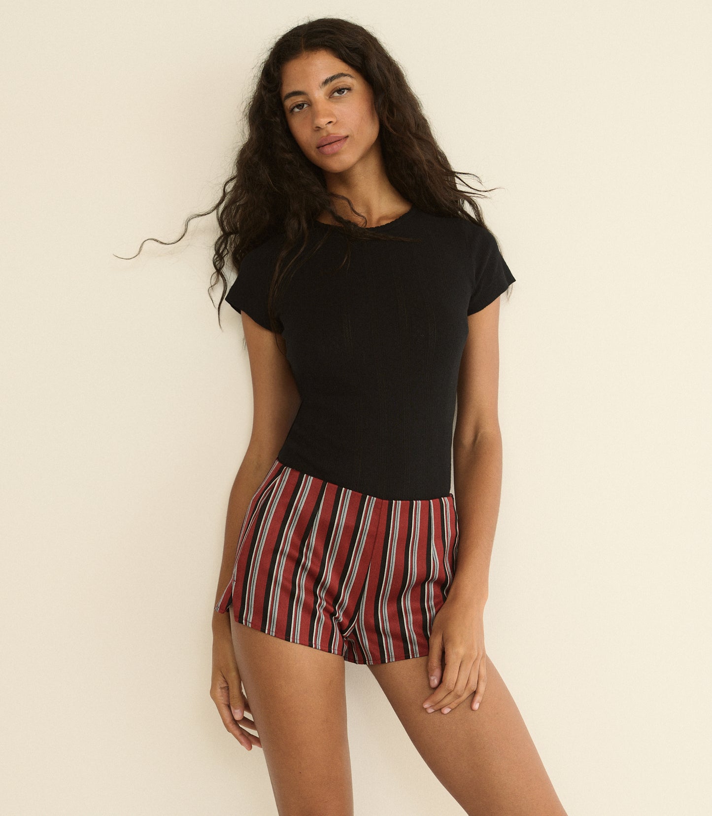 Woman wearing a black top and red striped shorts against a beige background