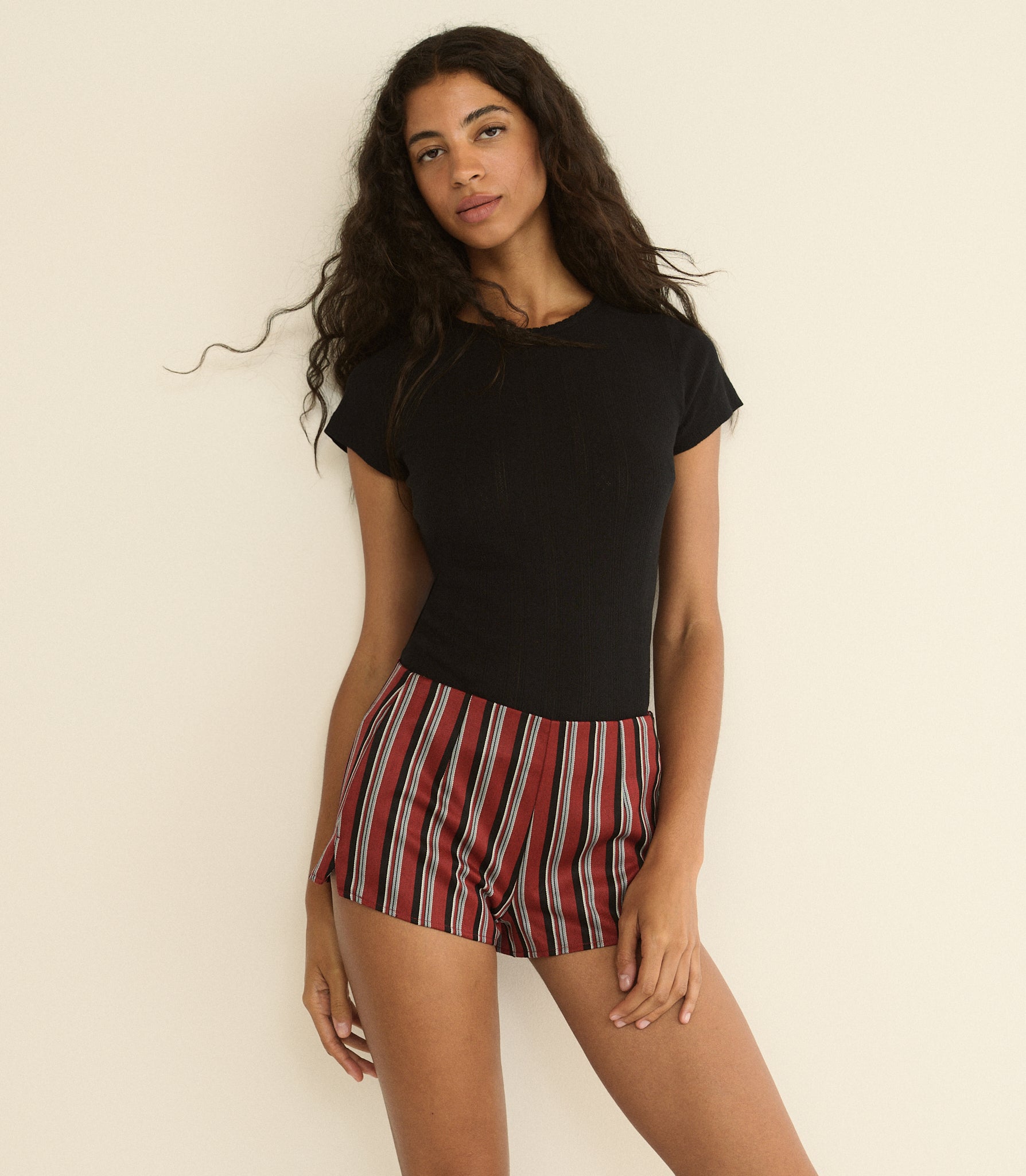 Woman wearing a black top and red striped shorts against a beige background