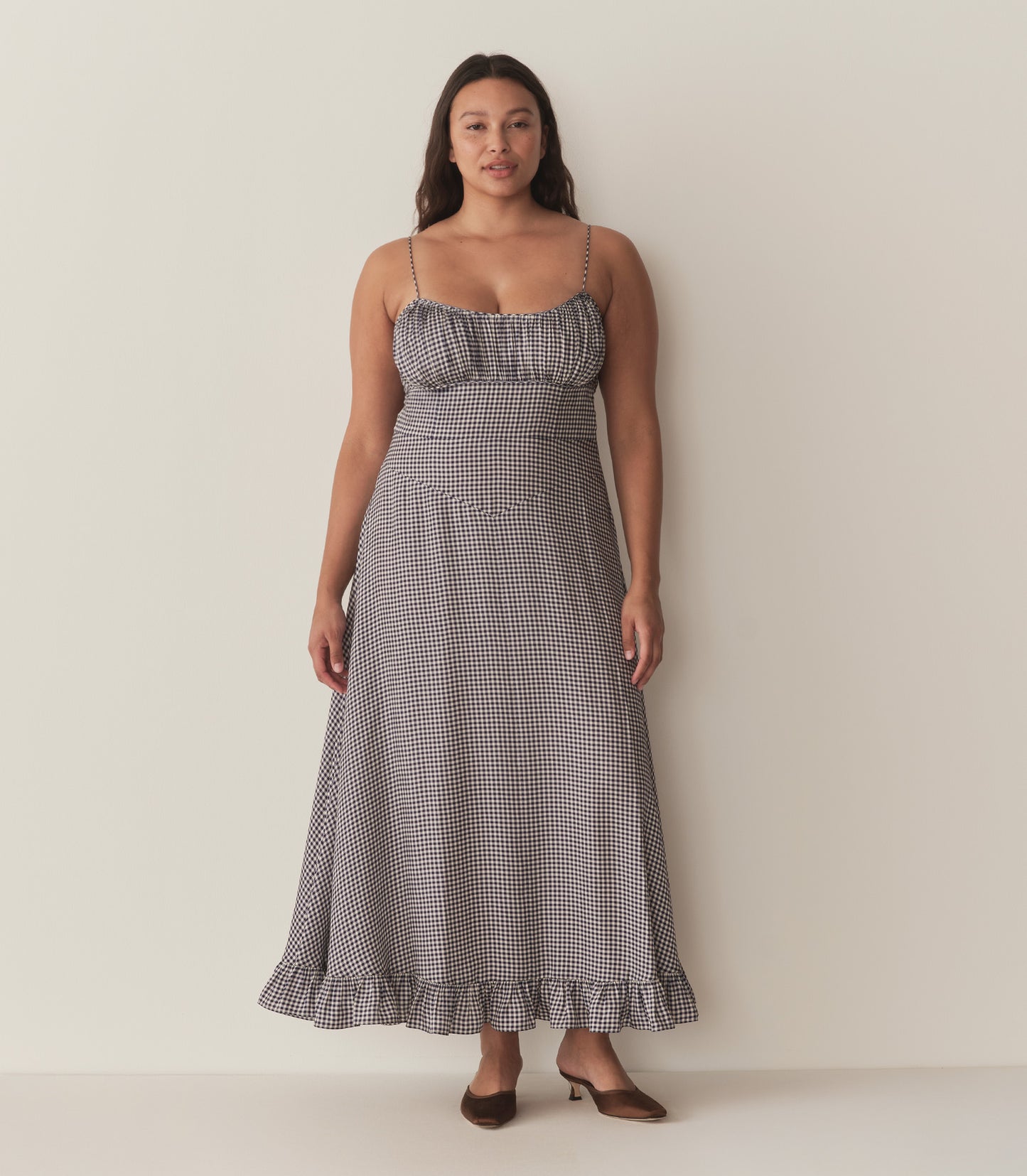 Alana wears the blue gingham Rosaria Dress and brown heels.