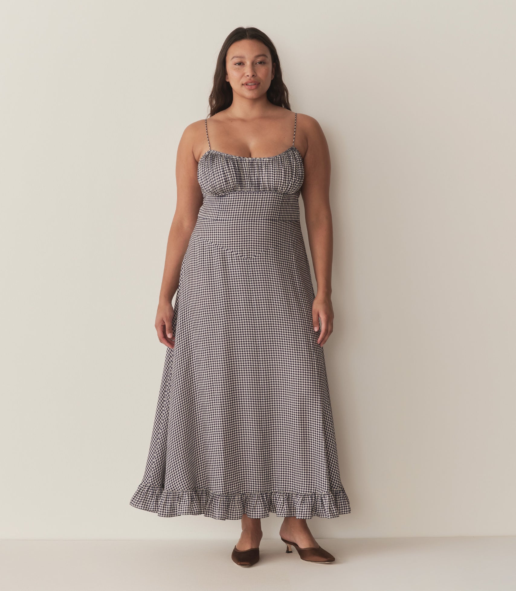 Alana wears the blue gingham Rosaria Dress and brown heels.
