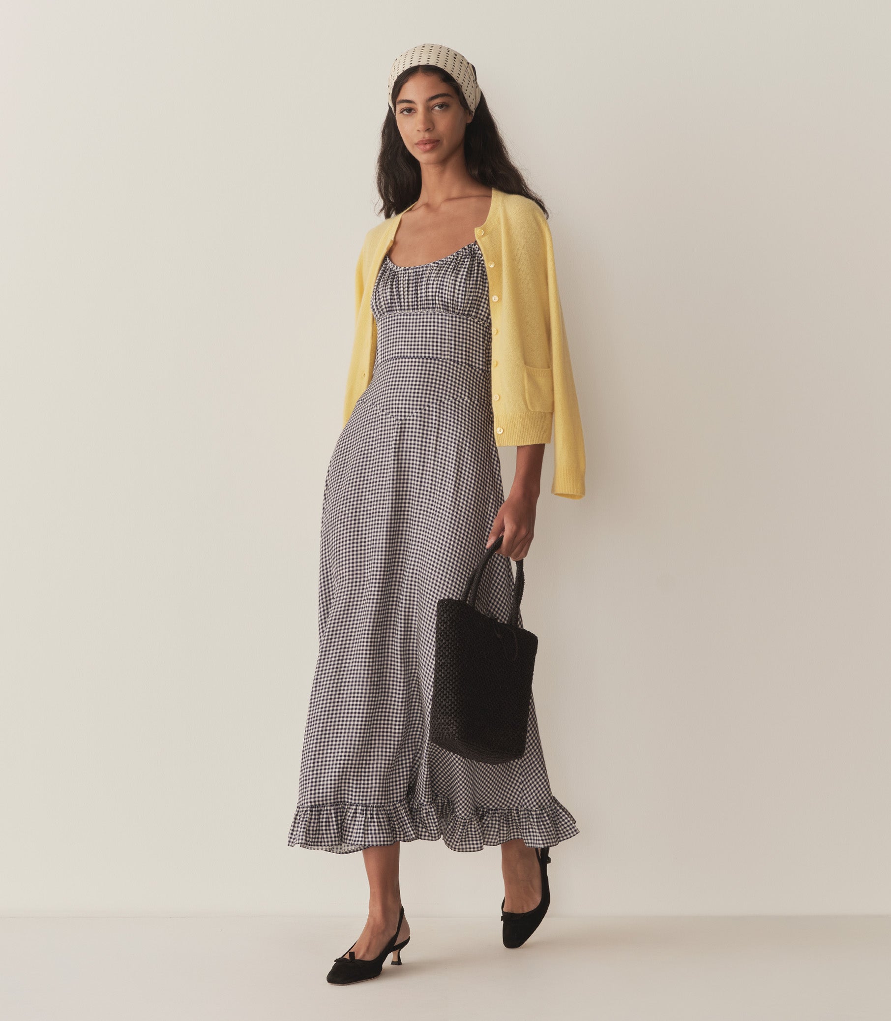 Rocio wears the blue gingham Rosaria Dress and a yellow cardigan draped over her shoulders. 3