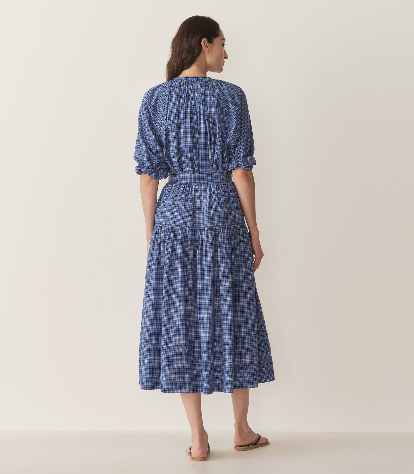 Bruna wears a blue and black checkered top and skirt with black flip flops.