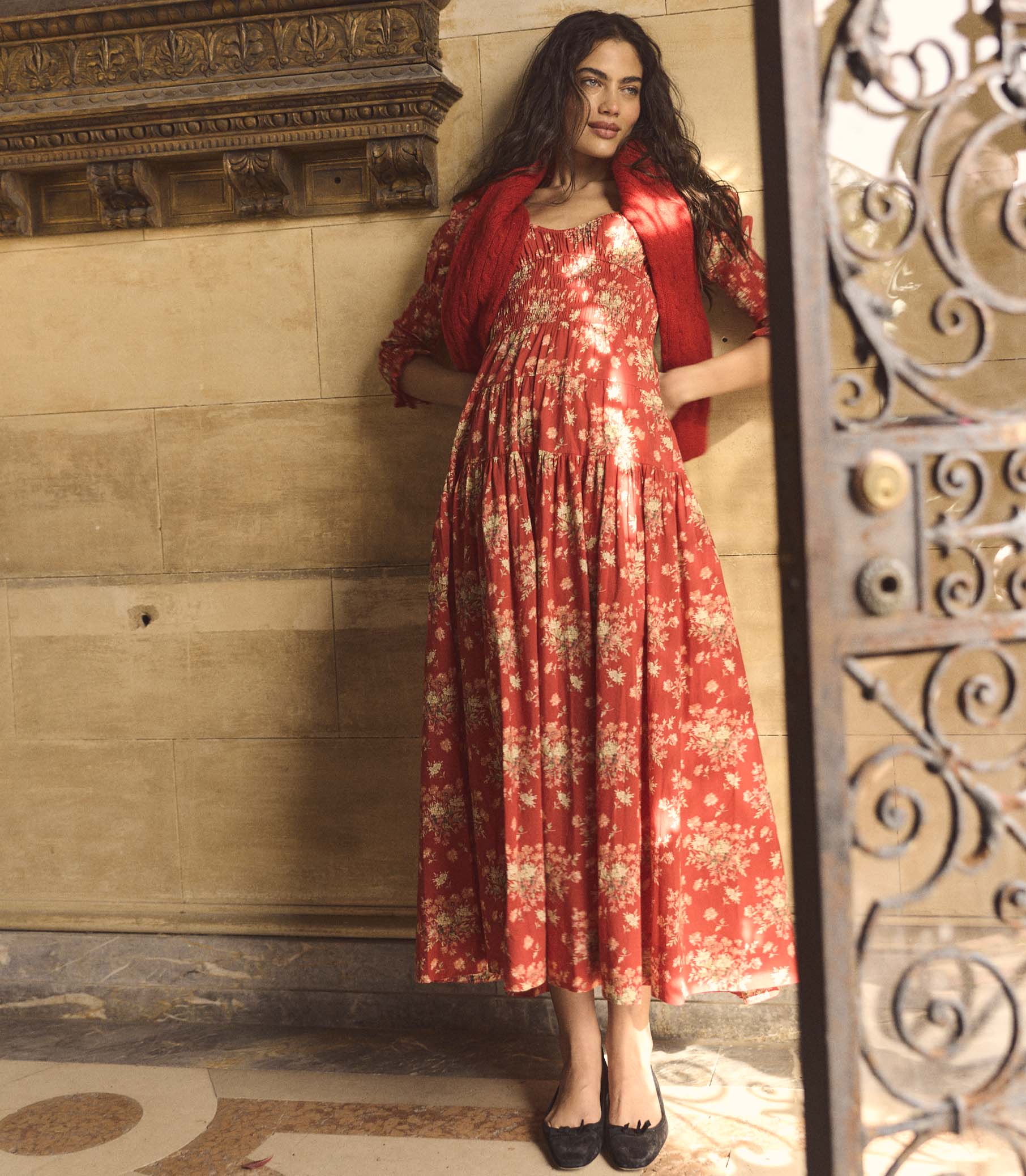 Woman wearing a red floral dress standing in a decorative interior setting.