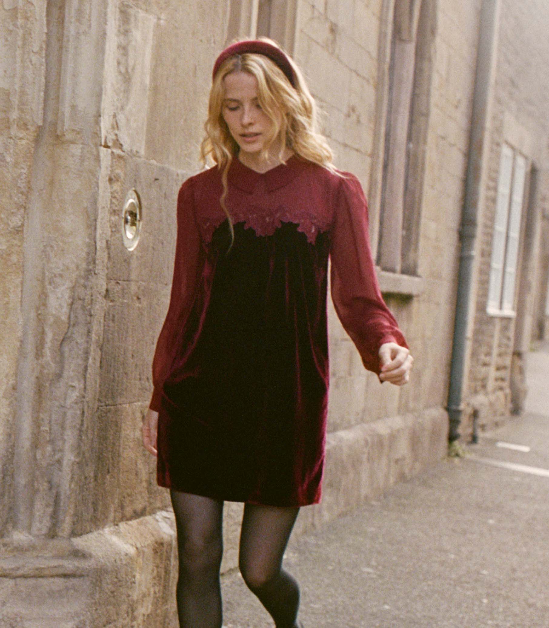 Woman in a burgundy velvet dress and matching velvet headband walking down a street.