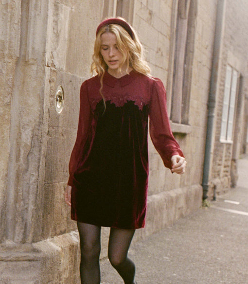 Woman in a burgundy velvet dress and matching velvet headband walking down a street.