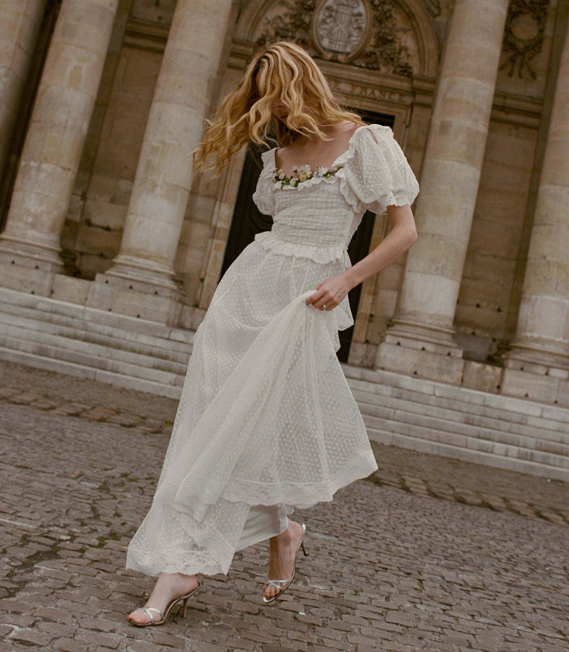 Woman in a white pin dot dress standing in front of classical architecture 1
