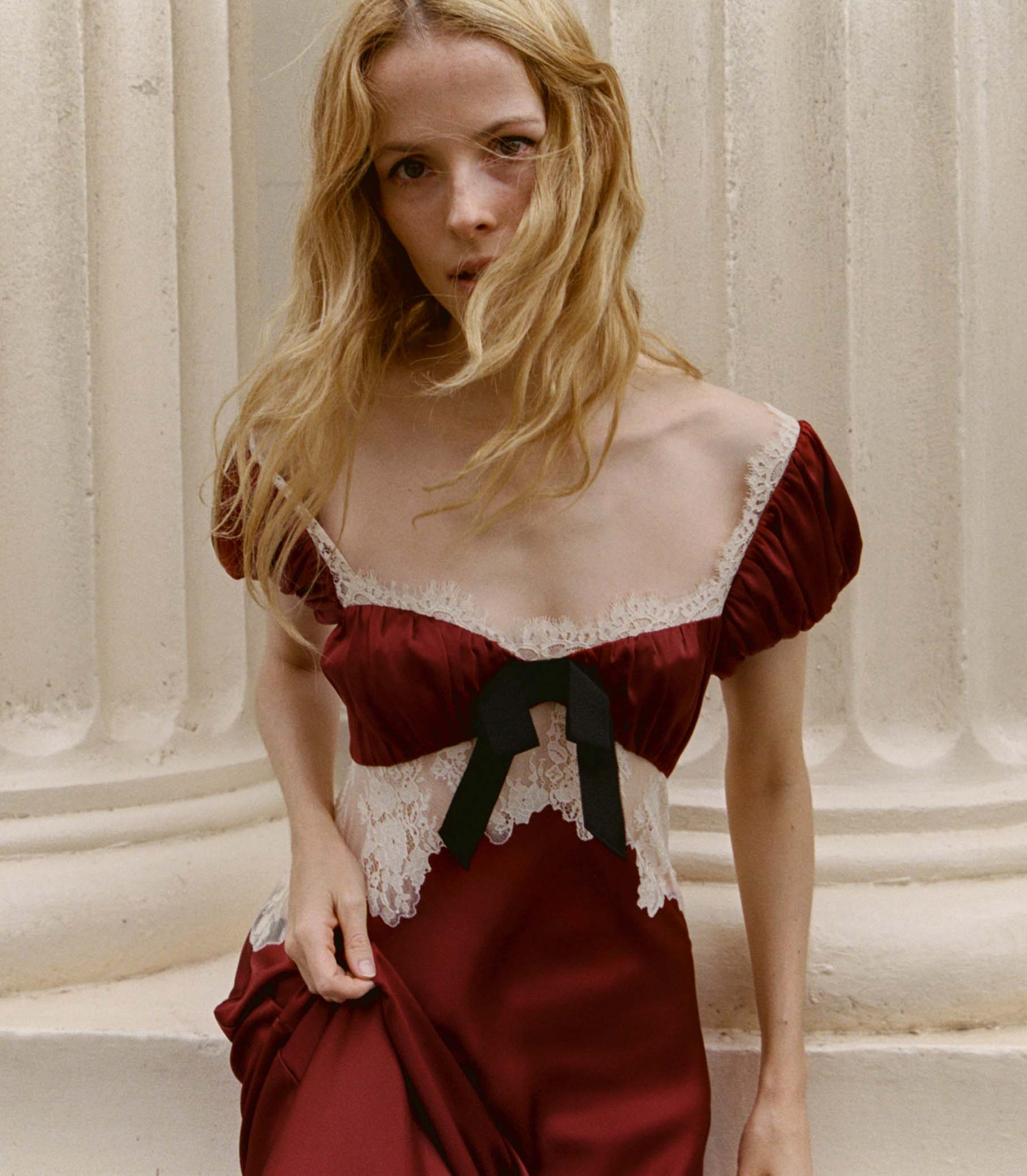 Woman wearing a red silk dress with lace details against a classical architecture background