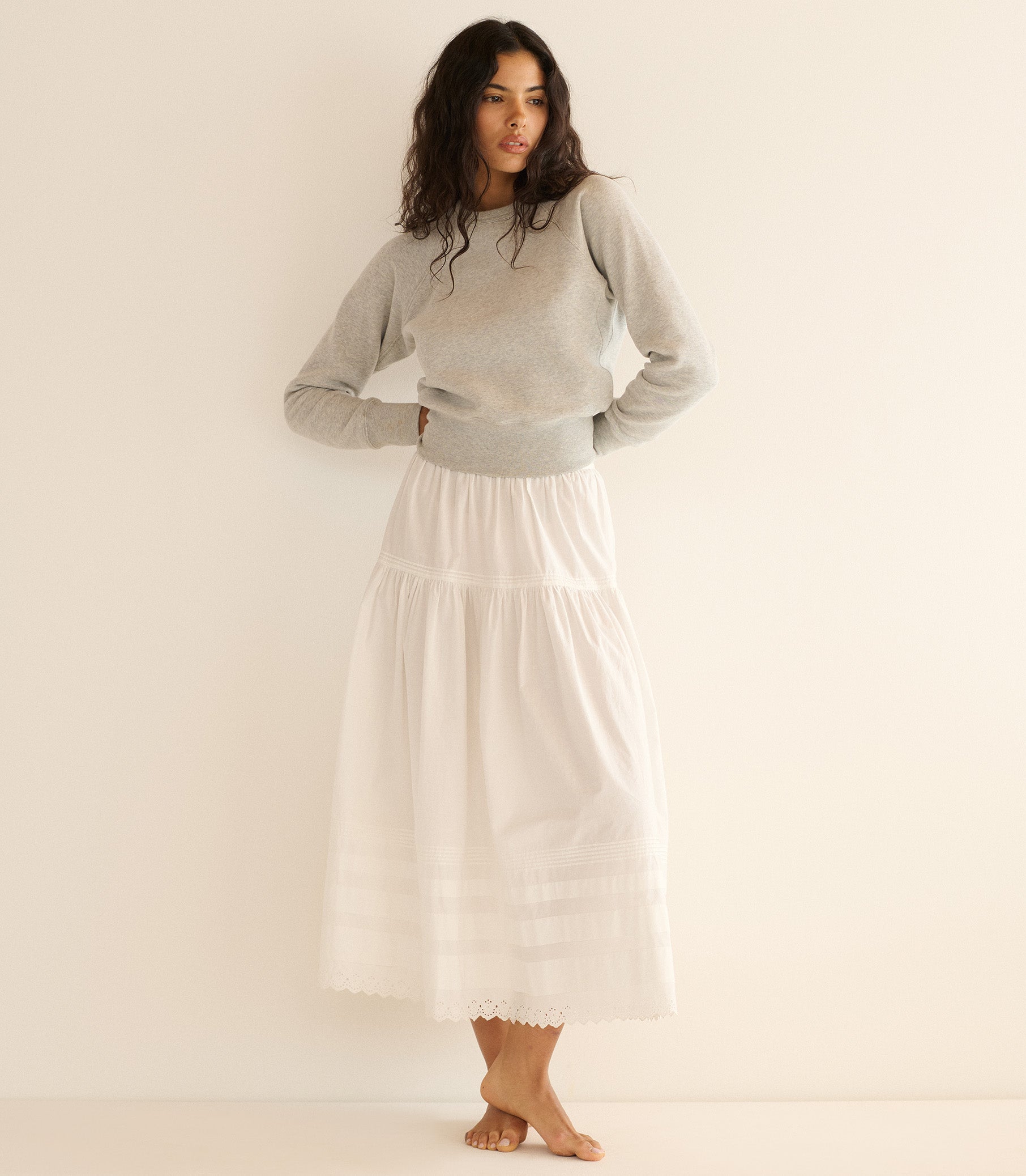 Woman wearing a gray sweater and white skirt against a plain background