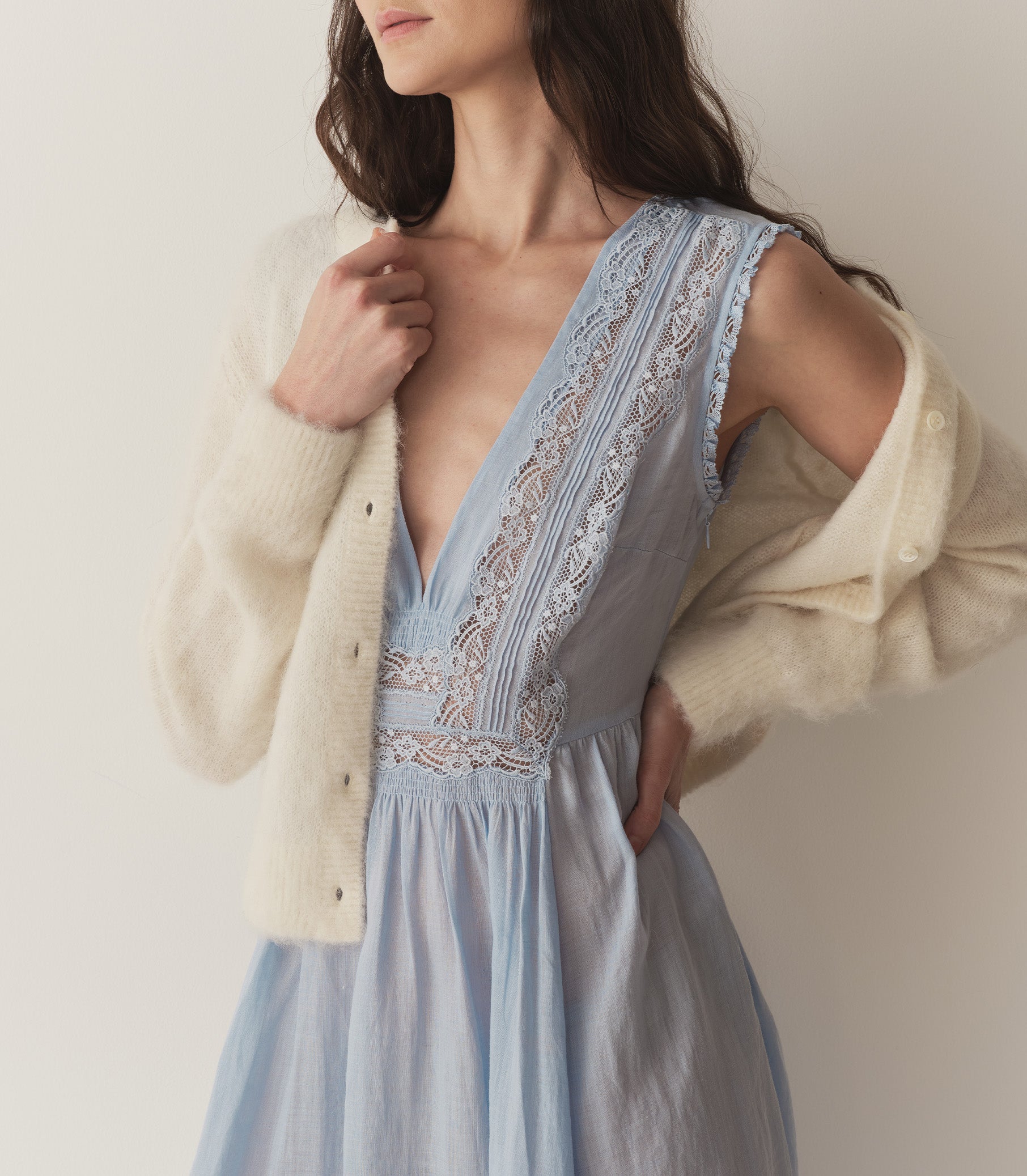 Bruna is wearing a long light blue sleeveless dress with lace details and light yellow kitten heels. 3