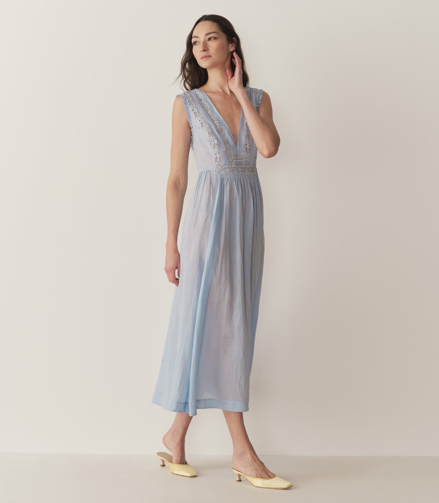 Bruna is wearing a long light blue sleeveless dress with lace details and light yellow kitten heels.