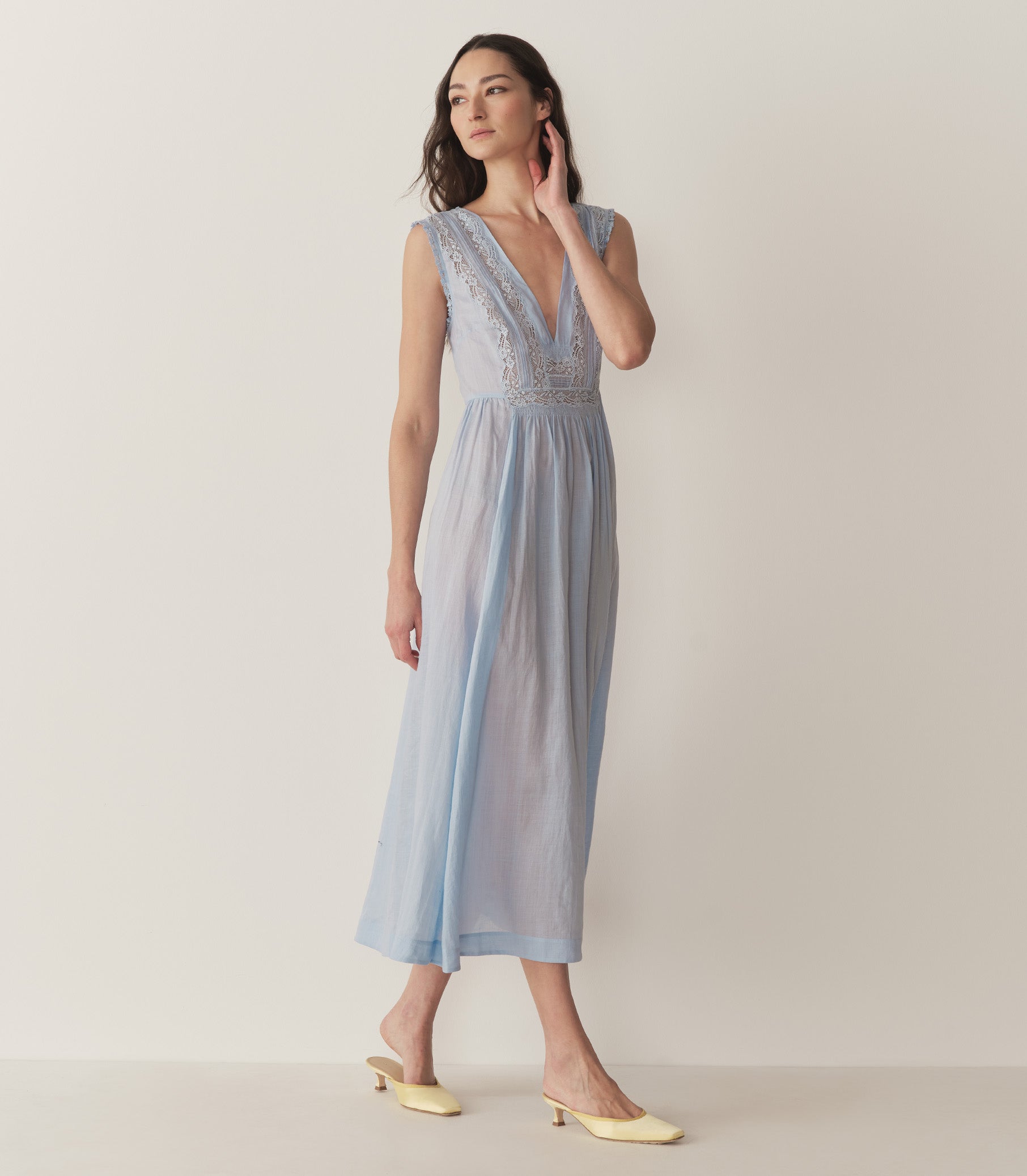 Bruna is wearing a long light blue sleeveless dress with lace details and light yellow kitten heels. 4