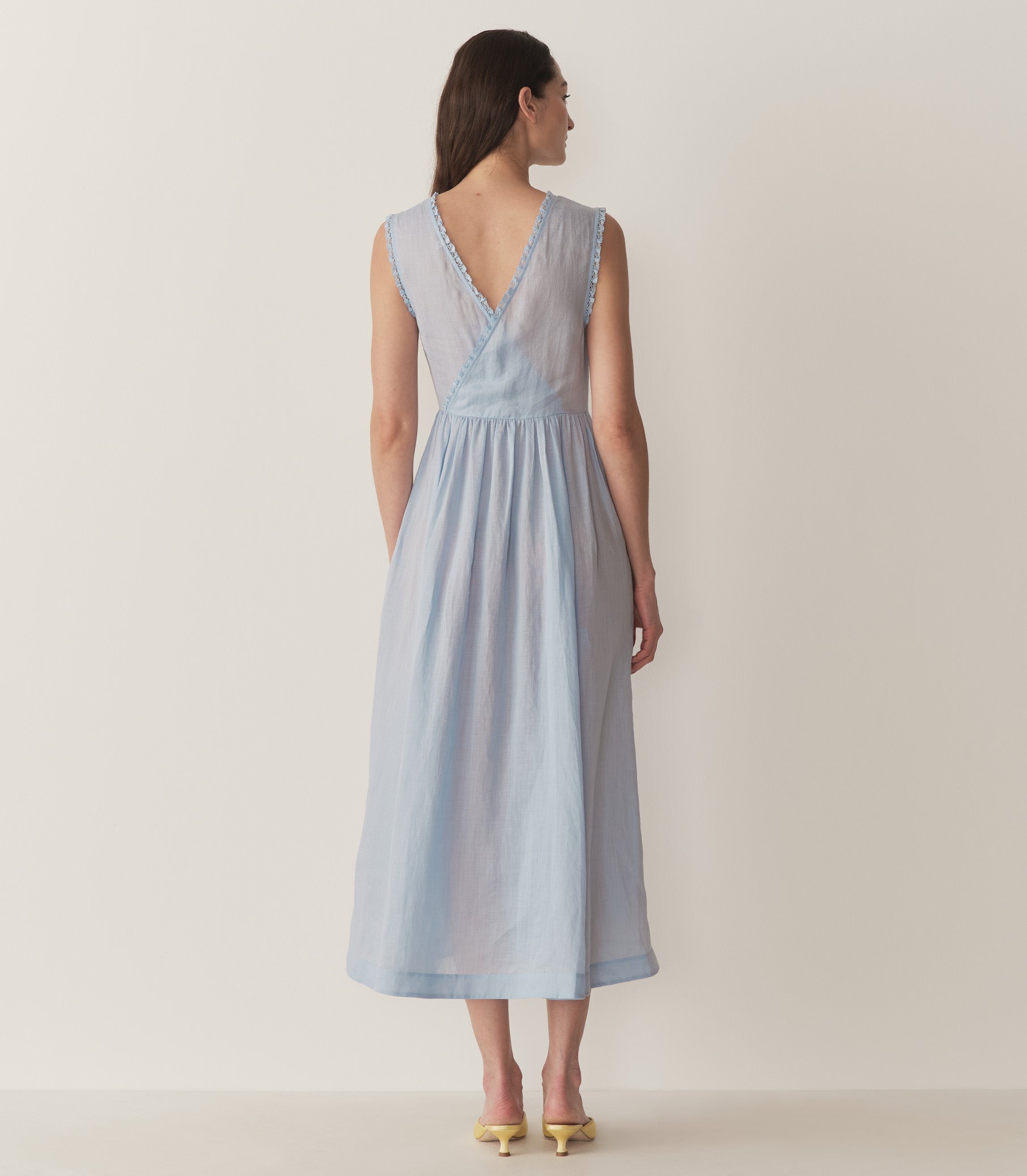 Bruna is wearing a long light blue sleeveless dress with lace details and light yellow kitten heels. 5