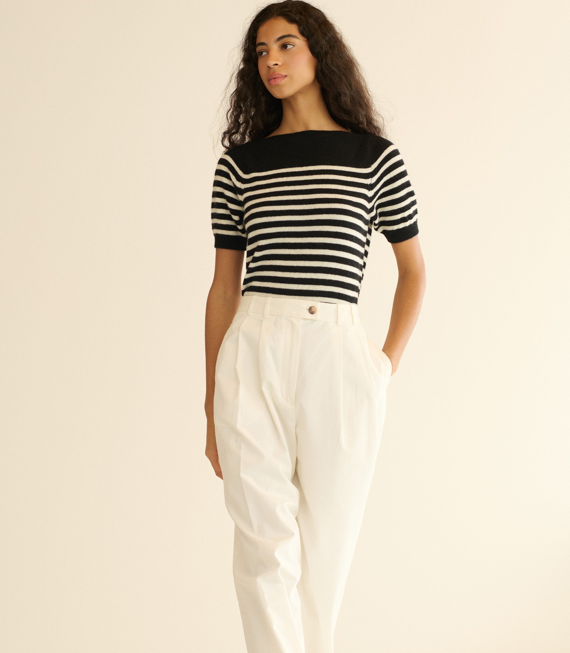 Woman wearing a black and white striped shirt with white pants on a beige background 1
