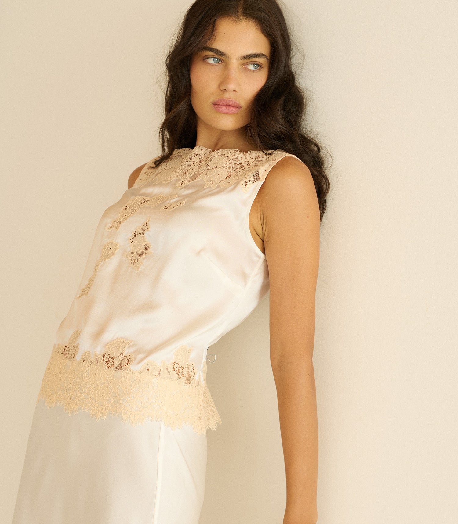 Woman wearing a white lace top against a plain background