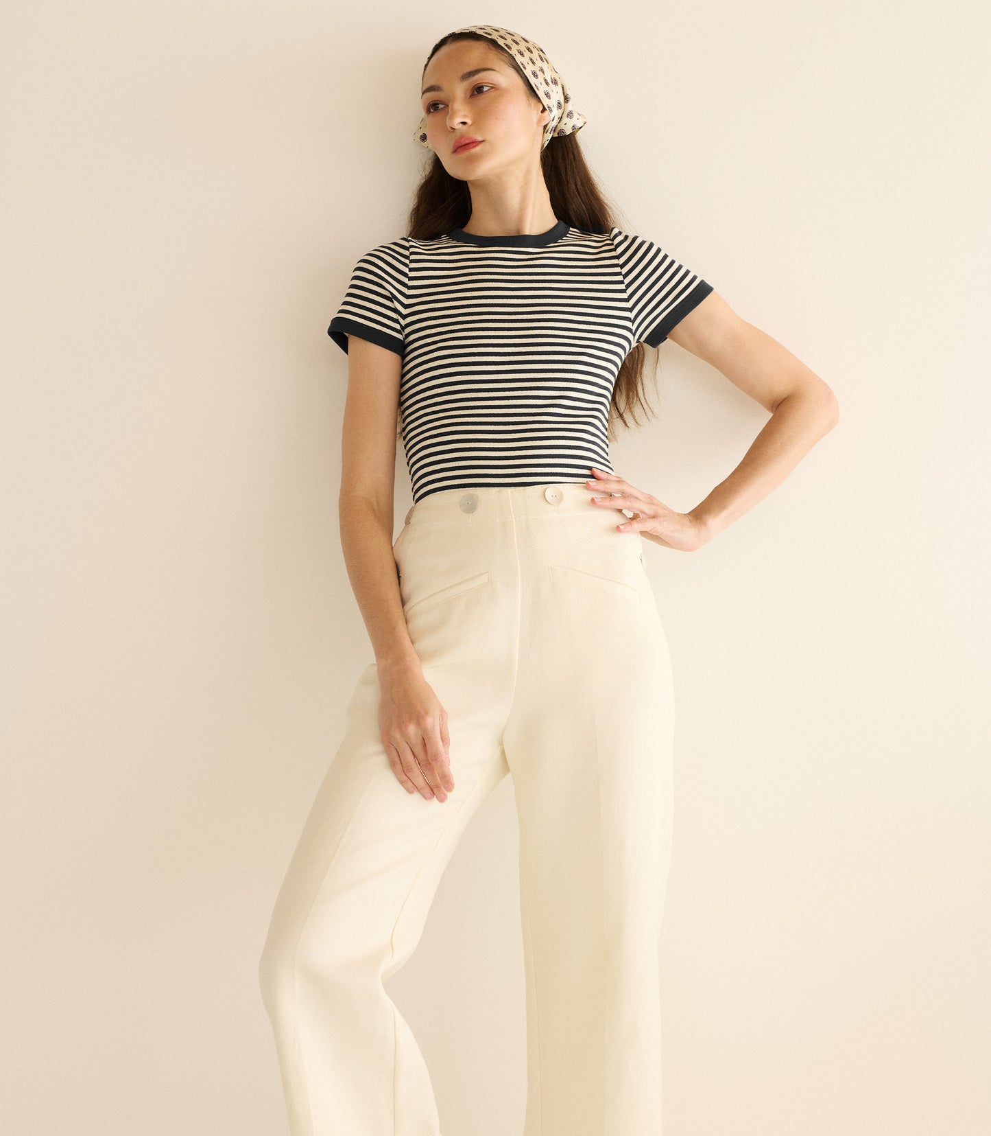 Woman wearing a black and white striped shirt and white pants against a plain background