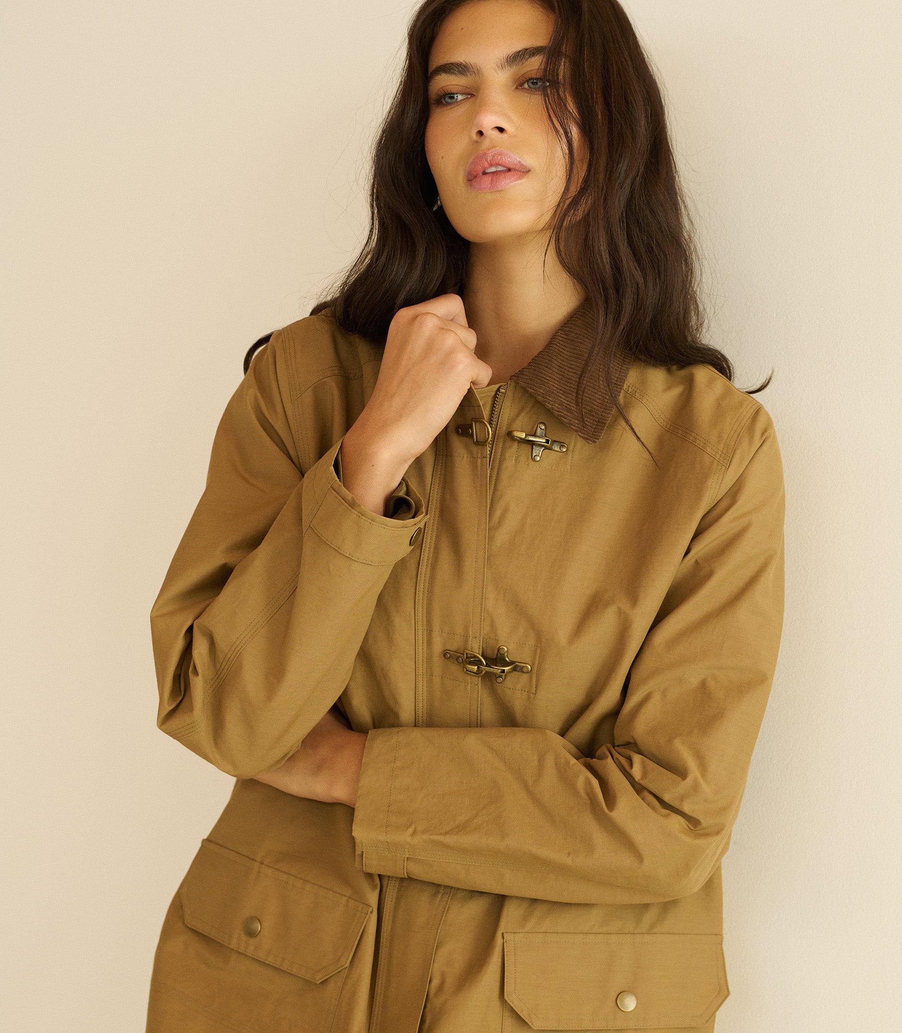 Woman wearing a brown jacket against a beige background